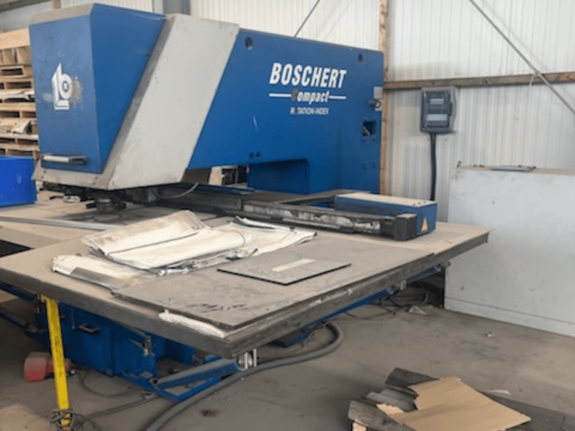 Töökojas asuv BOSCHERT COMPACT 1000 CNC-puurmasin, pildil on näha masina esivaade, kus laual on metallplaadid.