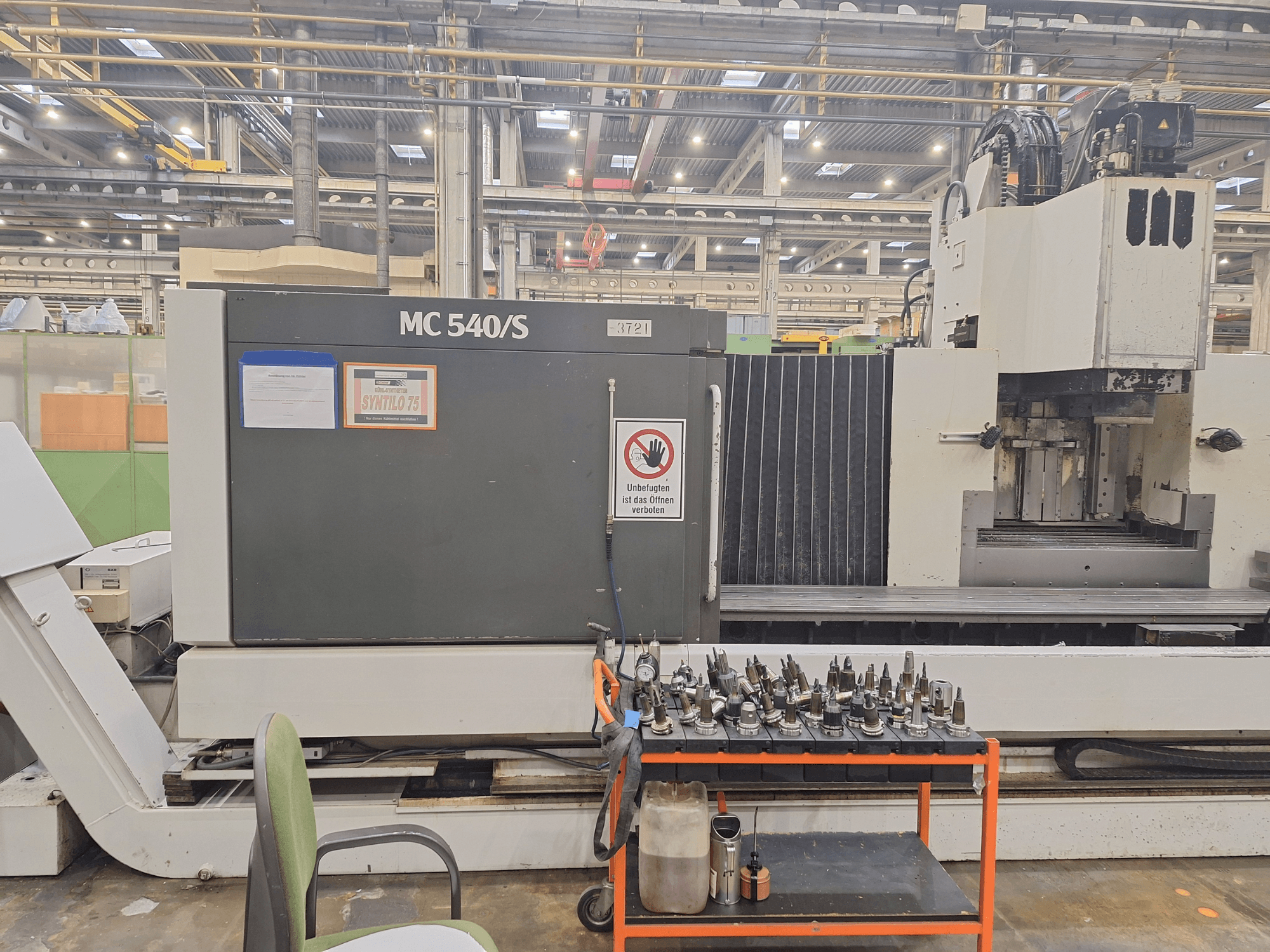 Vertikaalne töötluskeskus STAMA MC 540S töökojas, külgvaade koos tööriistahoidikutega vankril lähedal.