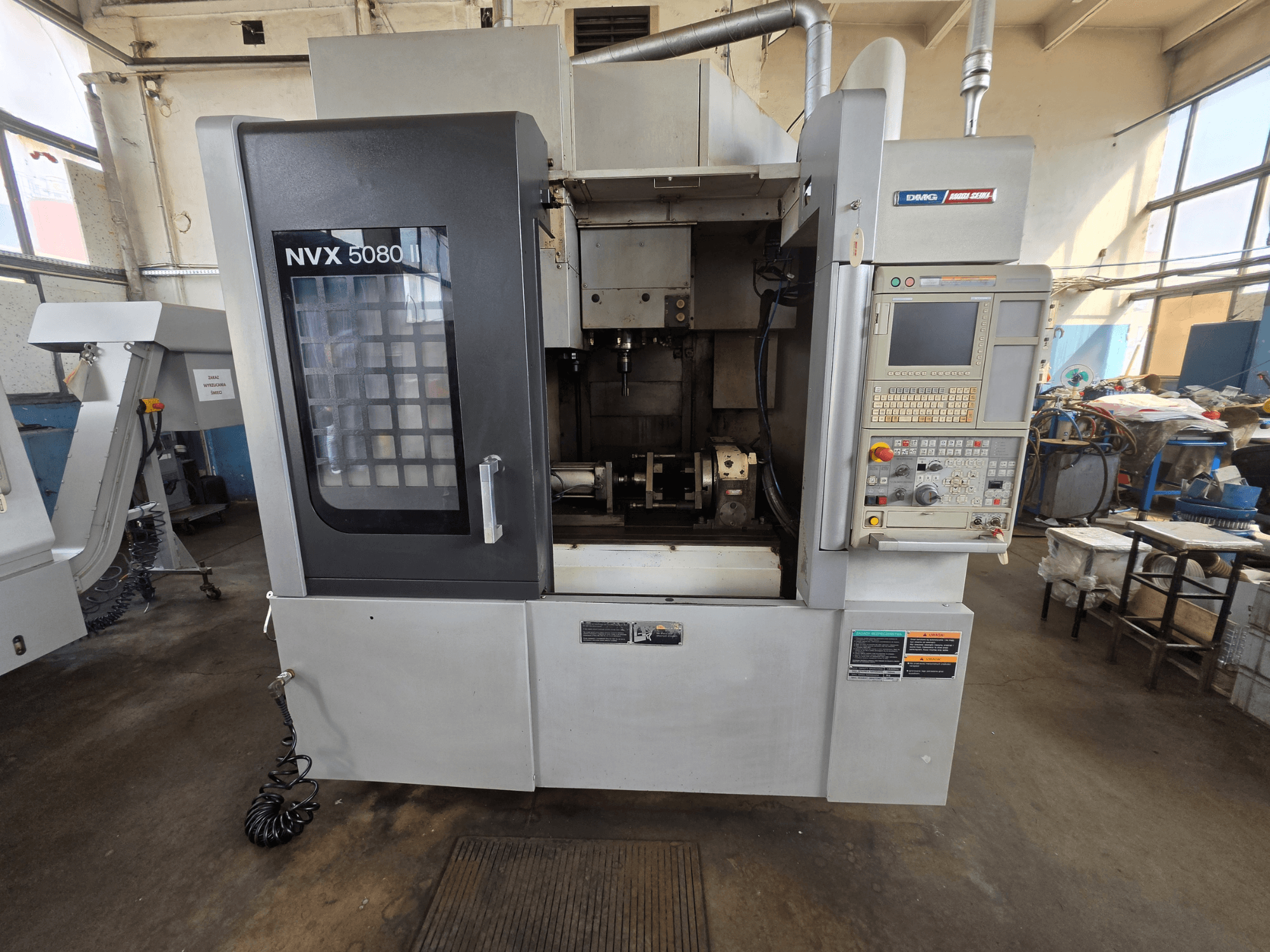 DMG Mori Seiki NVX 5080 II/40 vertikaalse töötlemiskeskuse esivaade koos juhtpaneeli ja läbipaistva aknaga, millest on näha töötlemisala.