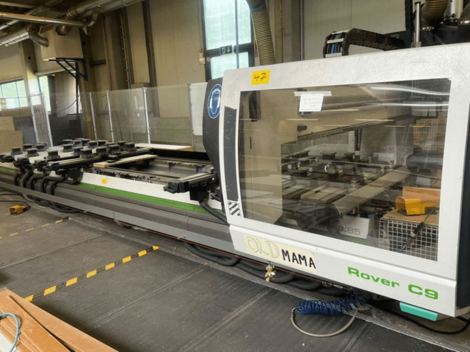 BIESSE Rover C 9.65 CNC-freesüsteem töökojas, külgvaates on näha juhtpaneel ja töölaud koos klambritega.