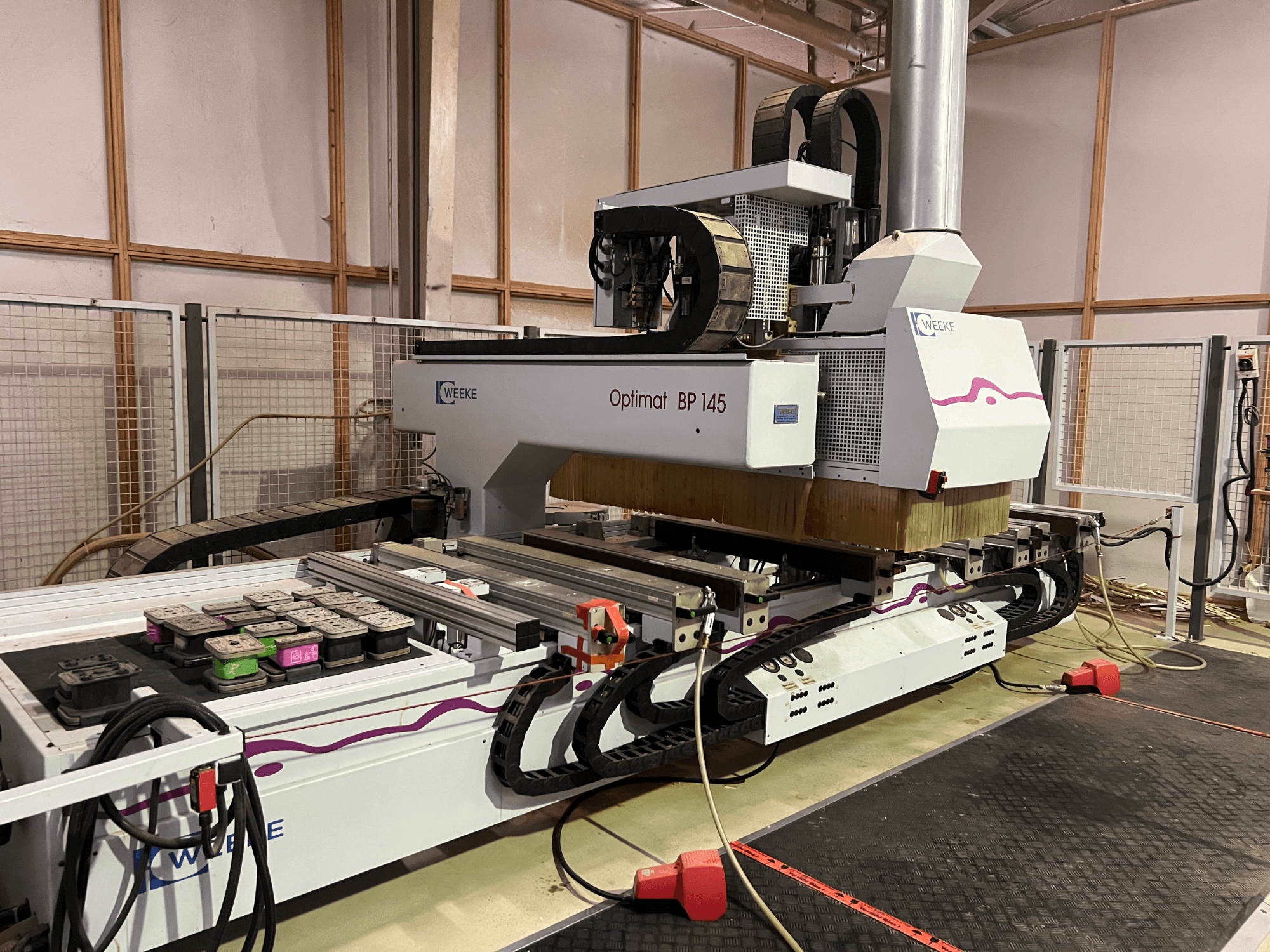 WEEKE Optimat BP 145 tehases, kus näidatakse CNC-masinat koos juhtnuppude ja kaablitega, küljelt vaadatuna.