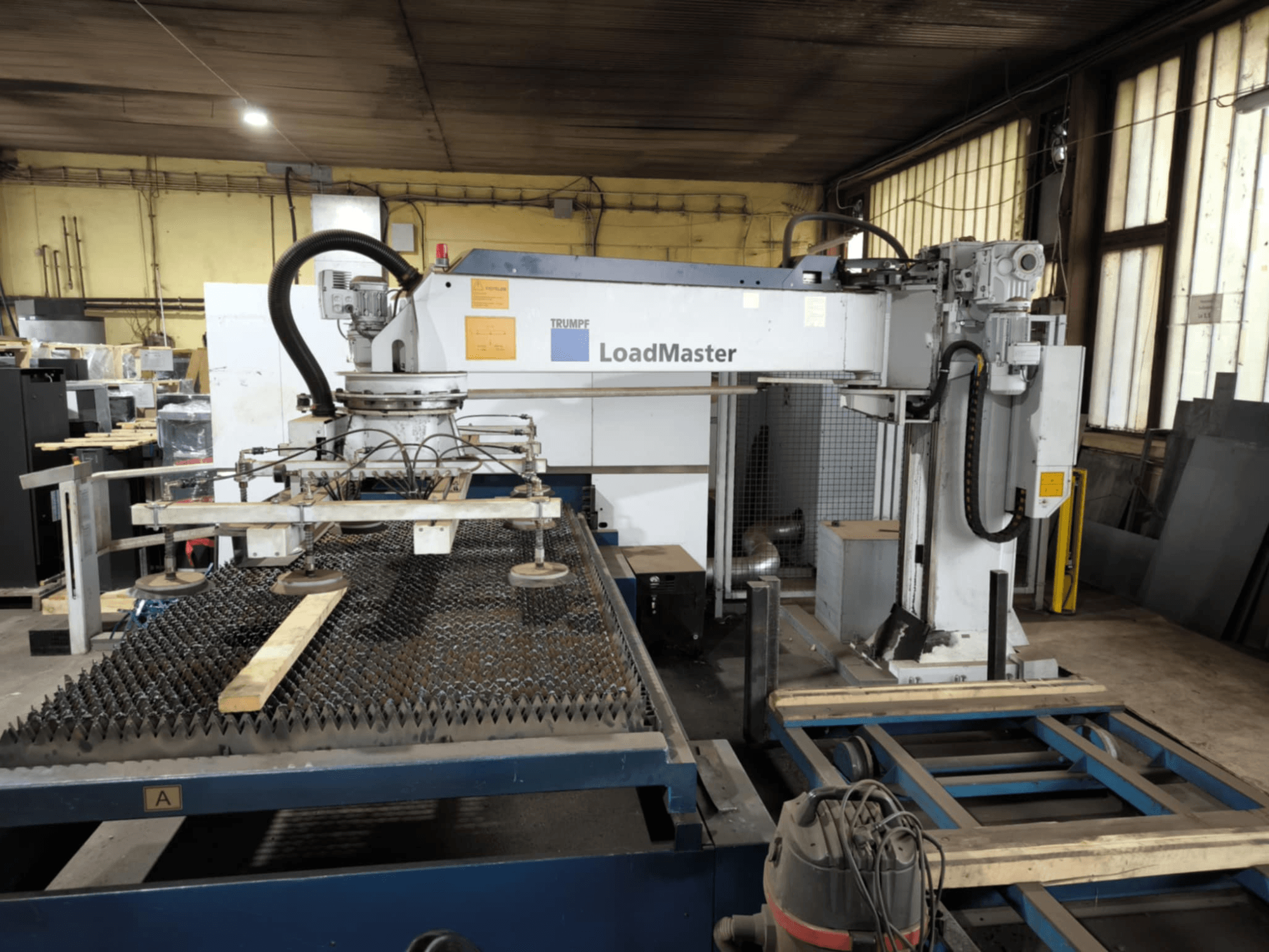 TRUMPF TRULASER 3030 FIBER lõikemasin, esiplaanil, kus näidatakse LoadMaster süsteemi ja mis on paigutatud riivitud töölauale.