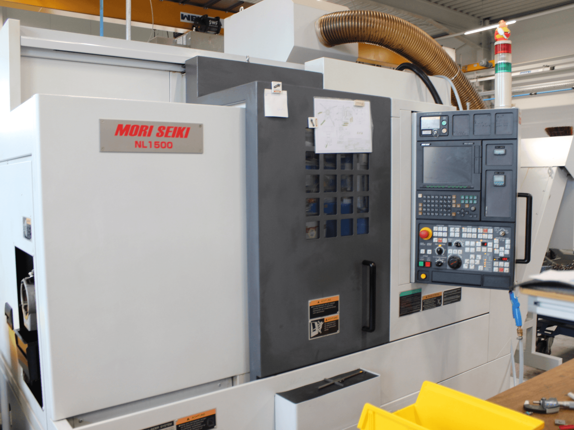 MORI SEIKI NL 1500 SY treimis- ja freesimiskeskus külgvaates, millel on juhtpaneel, tööohutuse sildid ja jahutussüsteem.
