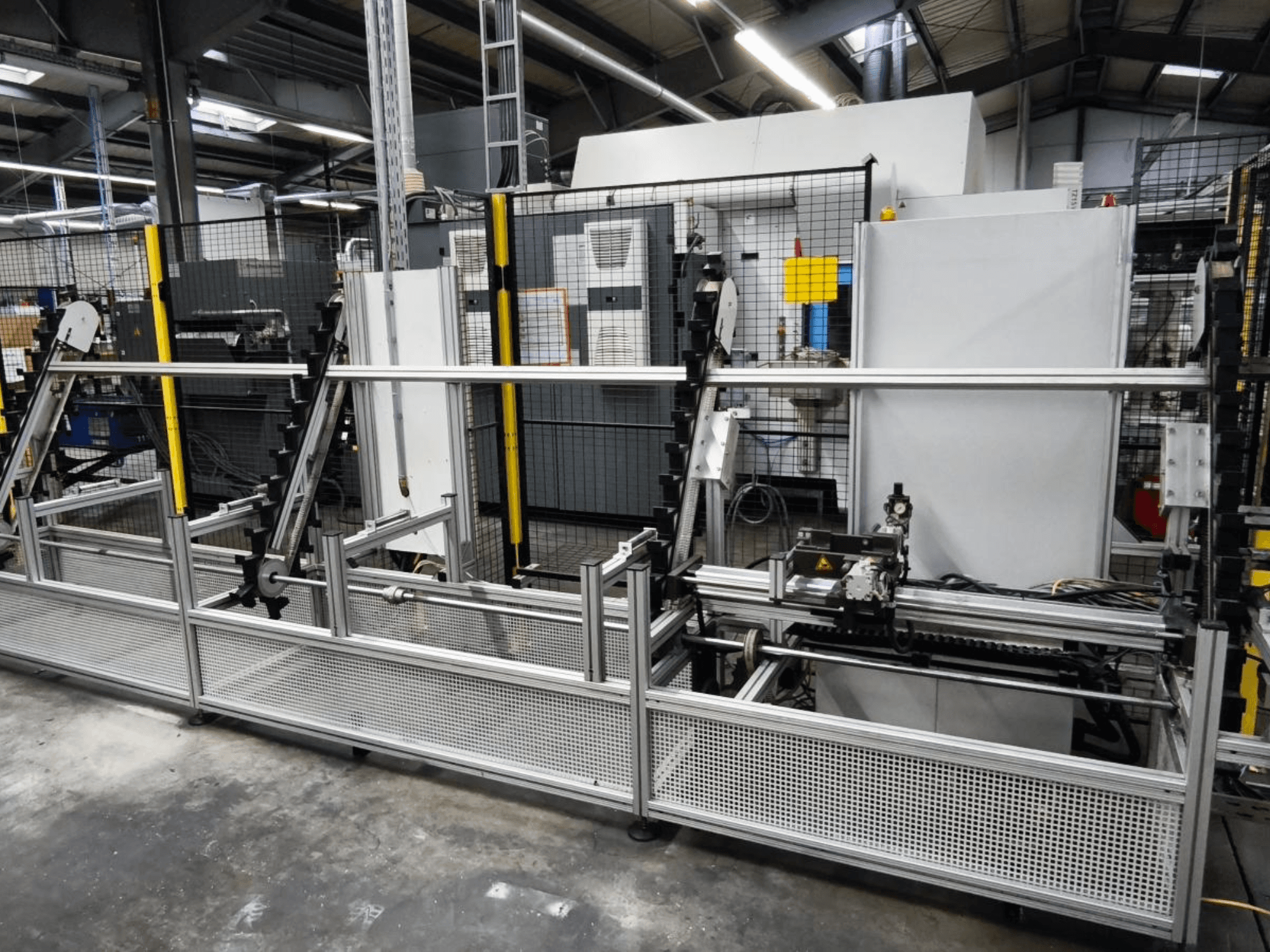 LOHMEIER Schräglademagazin töödeldavate detailide käitlemissüsteem esiplaanil, mis näitab selle metallkonstruktsiooni ja integreeritud mehaanilisi komponente.