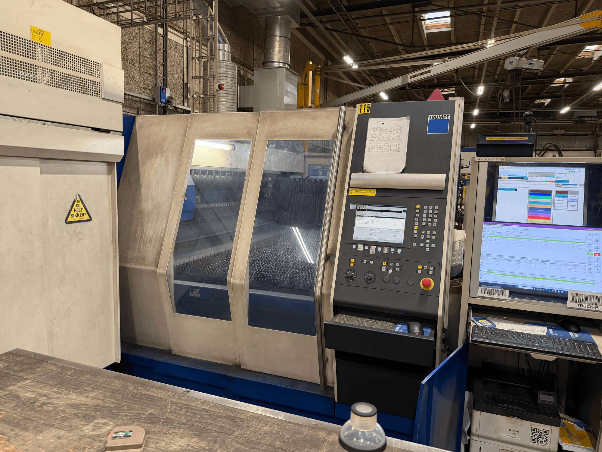 Trumpfi tööstusliku lasermasina esivaade koos juhtpaneeli ja digitaalsete näidikutega, mis on paigutatud tehase keskkonda.