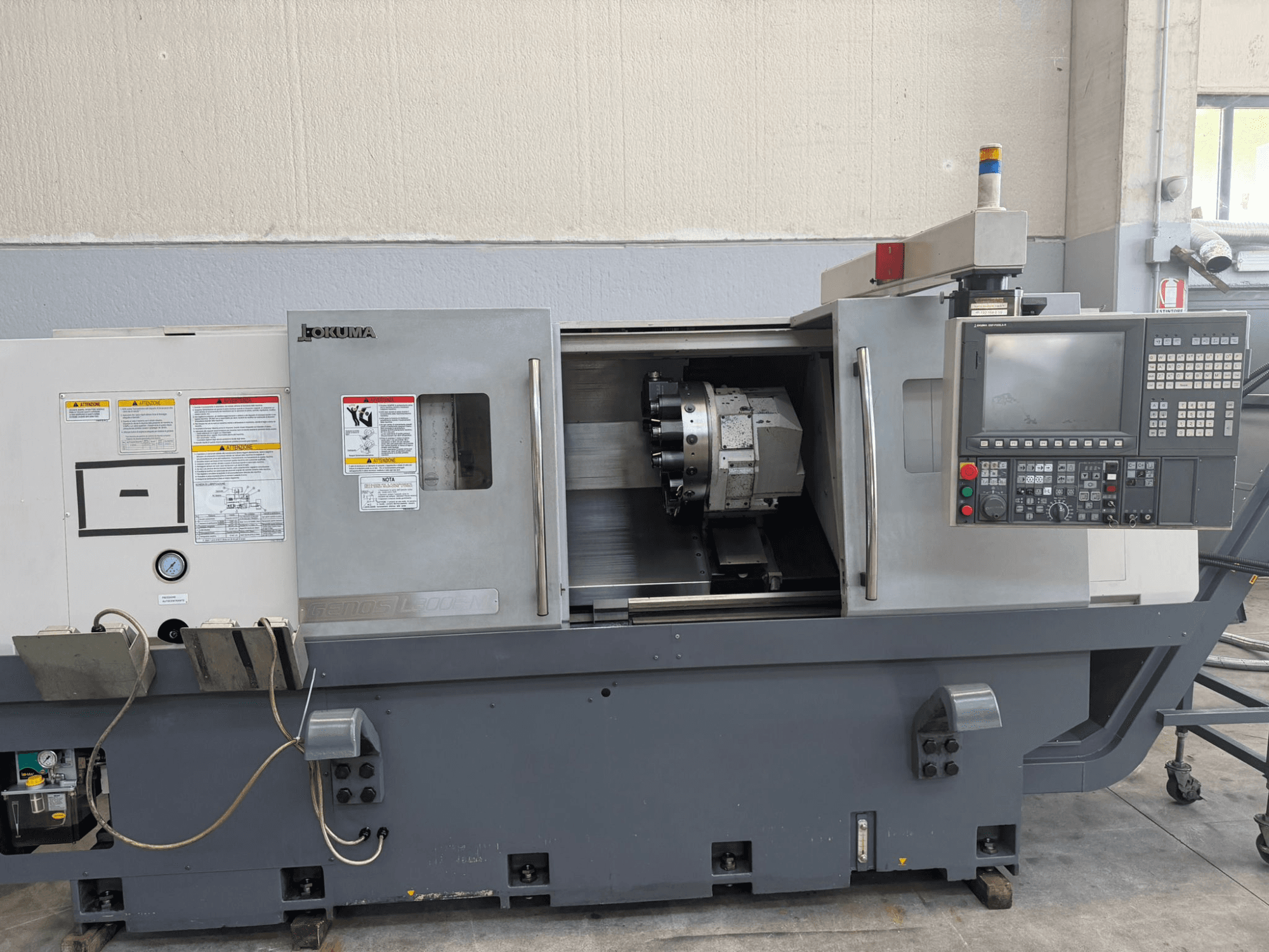 Okuma CNC-treipingi esivaade, kus on näidatud juhtpaneel, lõiketööriista hoidja ja küljel olevad ohutushoiatused.