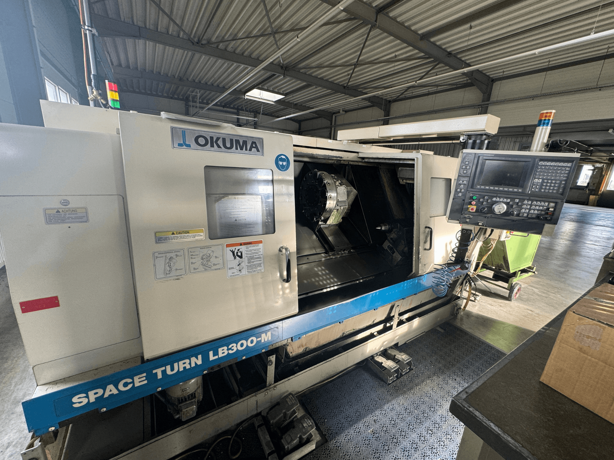 Okuma Space Turn LB300-M CNC-tööpink eesvaates, millel on juhtpaneel ja avatud uks, mis avab sisemise töötlemisala.