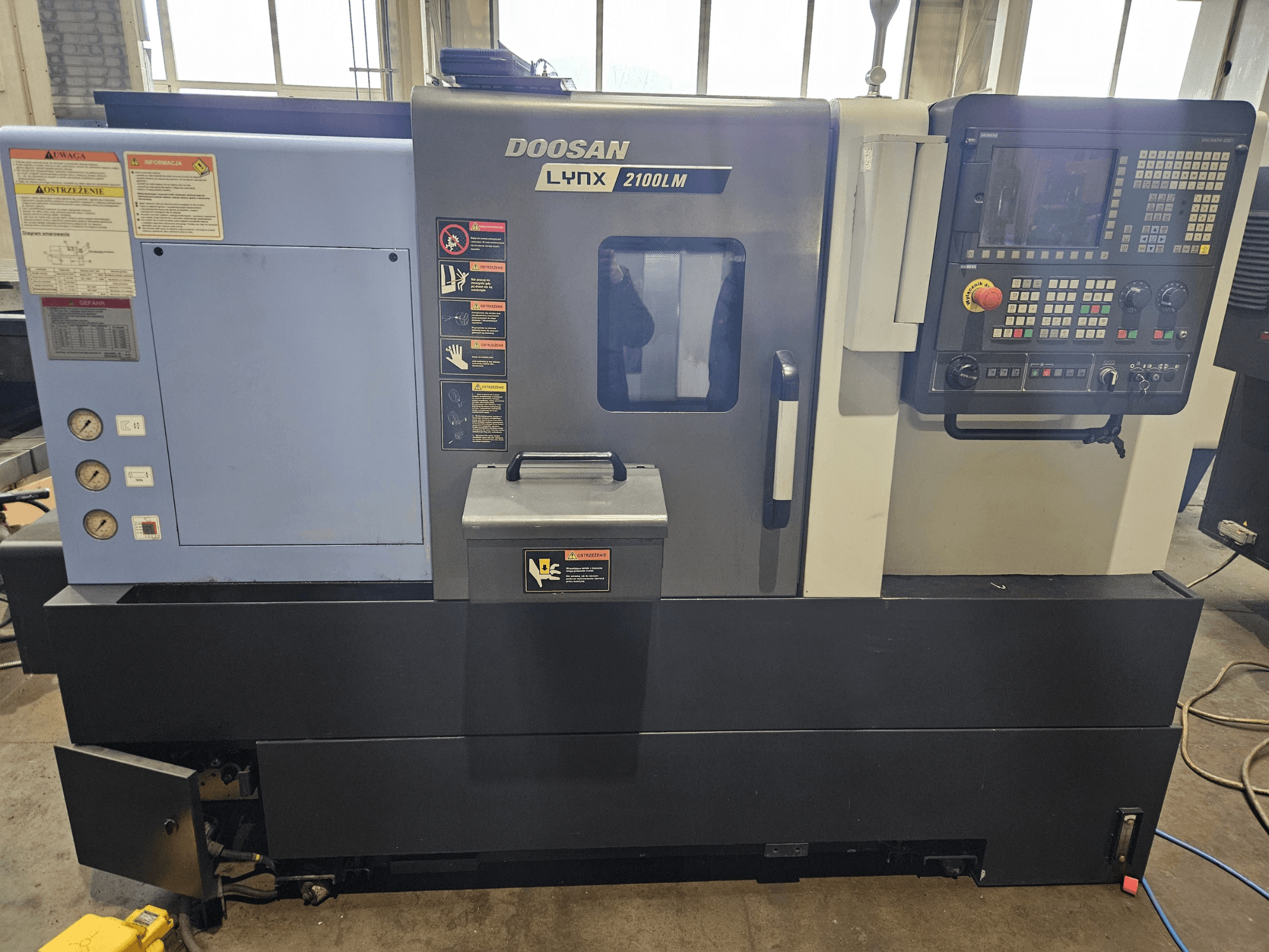 Doosan Lynx 2100LM CNC-tööpink, esivaade, juhtpaneel, õhurõhumõõturid ja ohutussildid nähtavad.