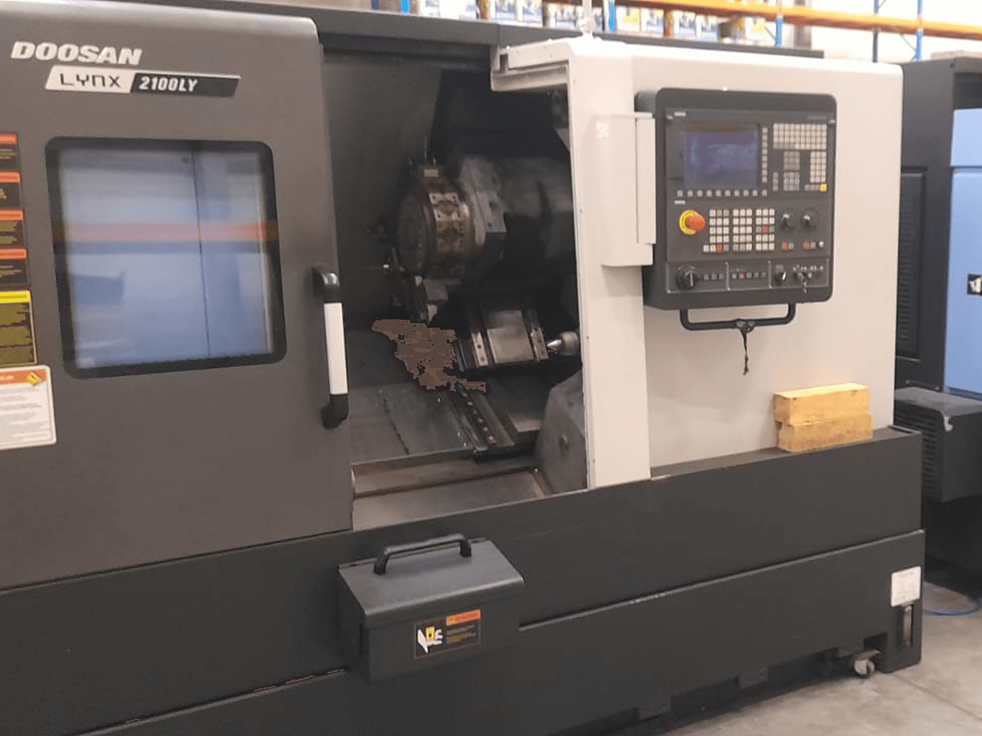 Doosan Lynx 2100LY CNC-tööpink, esiplaan, kus on näidatud juhtpaneel, tööriistahoidja ja sisemine tööruum; näha on tehnilised sildid.