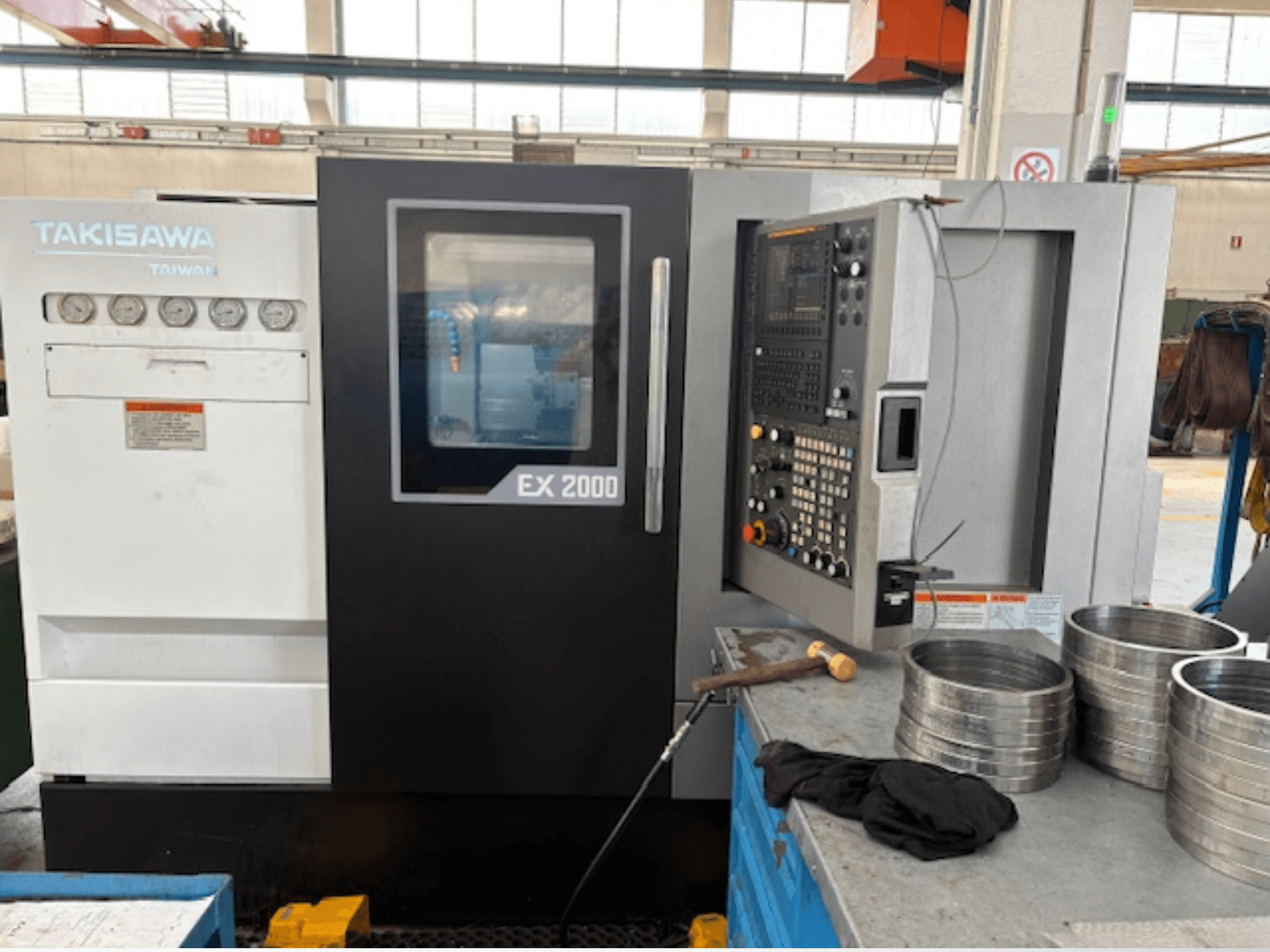 Takisawa EX 2000 CNC-tööpink, esiplaan, kus on juhtpaneel, mõõteriistad ja metallosad töökoja laual.