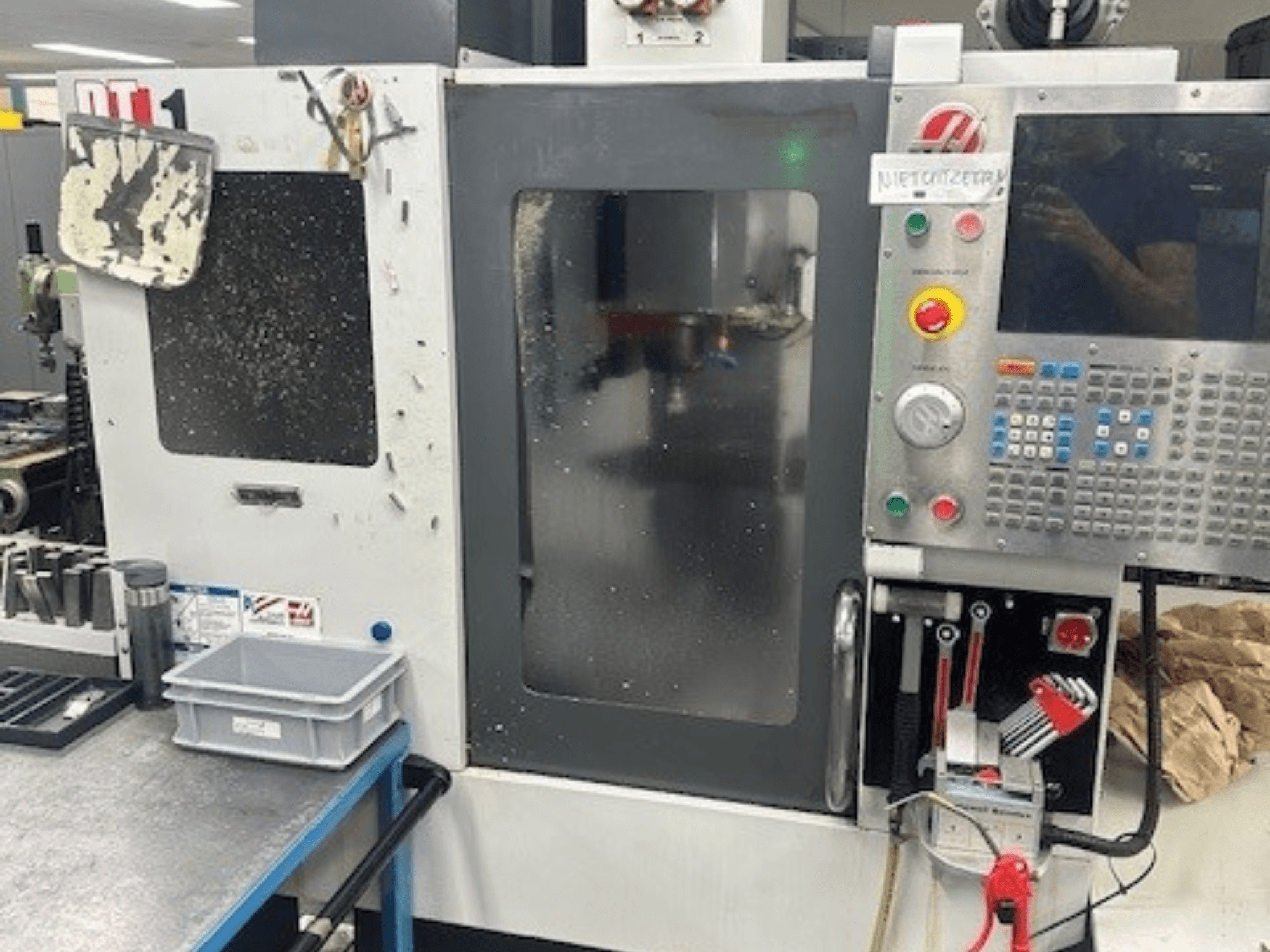 Haas DT-1 vertikaalne töötlemiskeskus, esikülg, juhtpaneel, nähtav mustus ja tööriistakast töölaual.