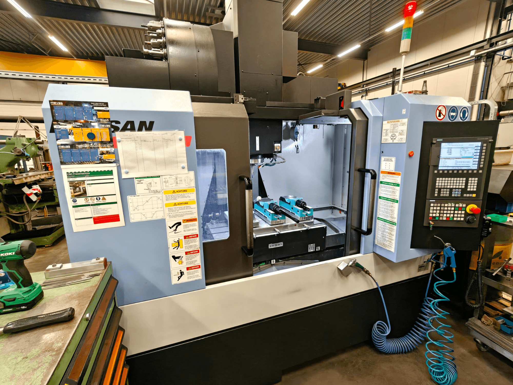DOOSAN DNM 400 II vertikaalne töötluskeskus töökojas, kus on juhtimisseadmed, tööriistahoidjad ja ohutusmärgid, esiplaanil.