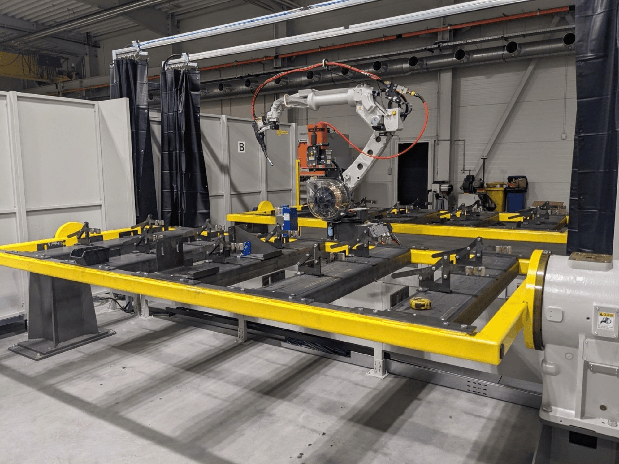 PANASONIC TAWERS TM-2000WG3 robotkäe esivaade, mis on paigutatud kollase töölauda kohale, millel asuvad kokkupanekuks mõeldud metallosad.
