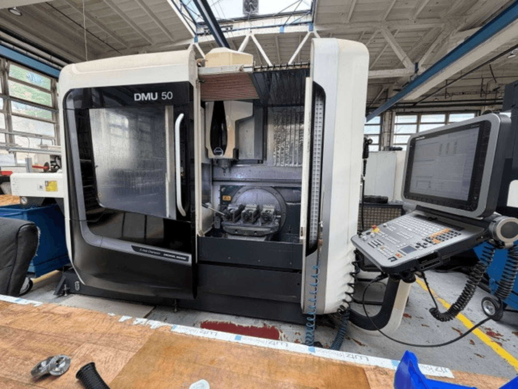 DMG MORI DMU 50 kolmanda põlvkonna vertikaalne töötlemiskeskus, vaade eestpoolt, avatud uksega, nähtav CNC-juhtpaneel ja töötsoon sees.