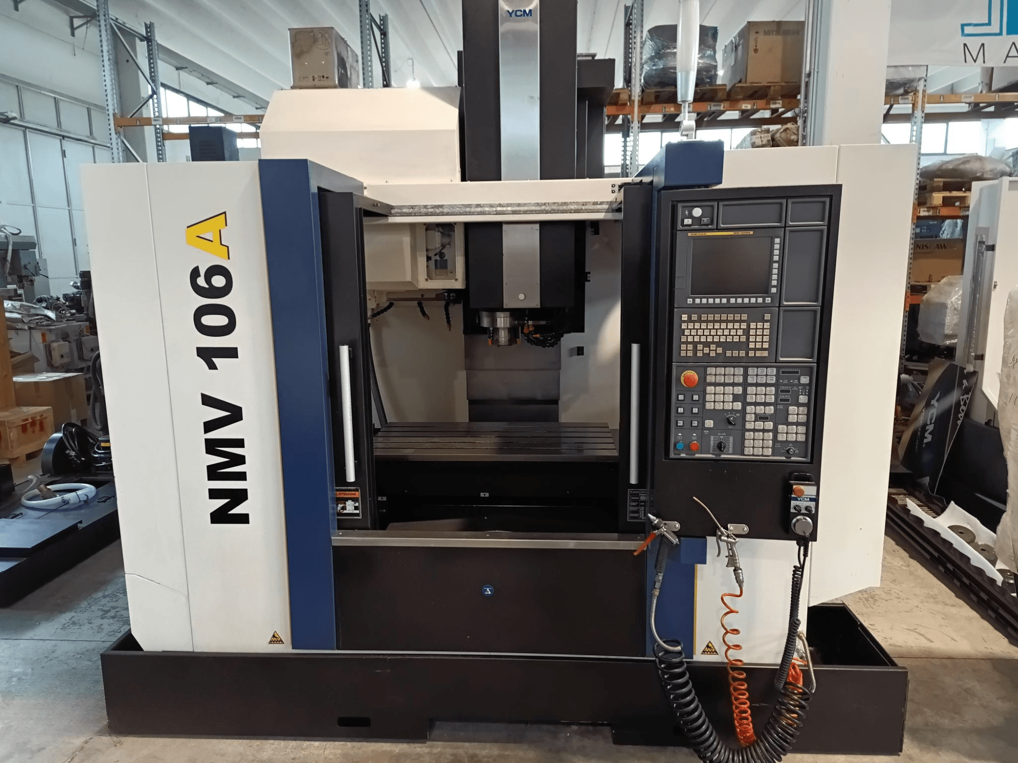 YCM NMV 106A töötluskeskus, esiplaan, millel on juhtpaneel koos nuppude ja jahutusvedeliku voolikutega.