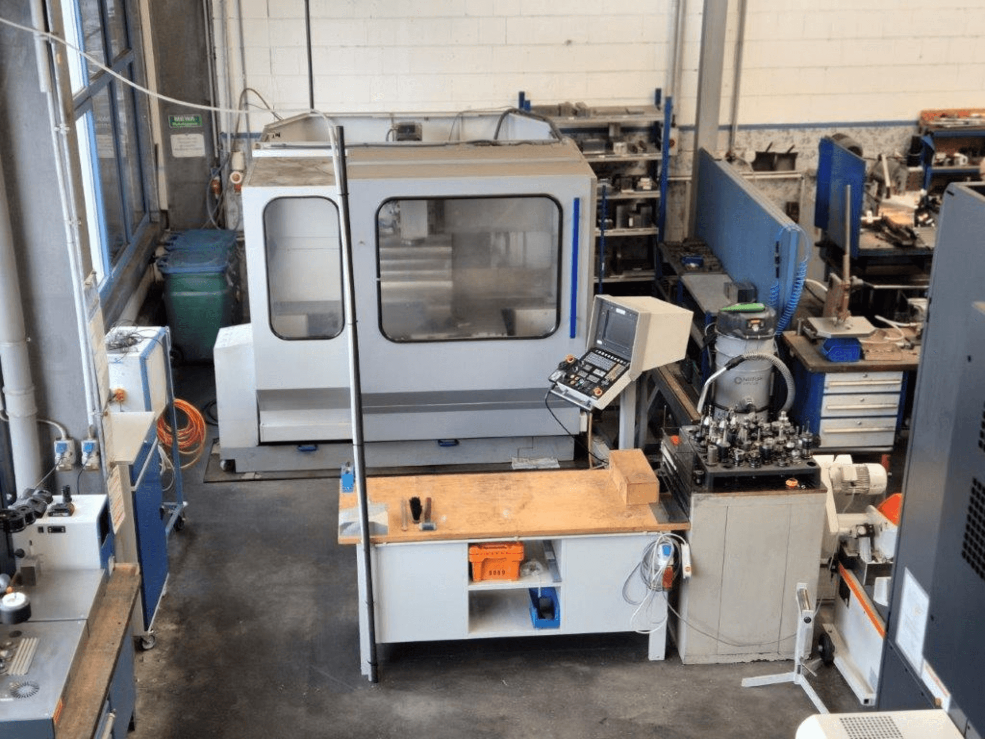 CNC-freesimispink töökojas, esiplaanil, taustal on näha juhtpaneel, tööpind ja tööriistad.