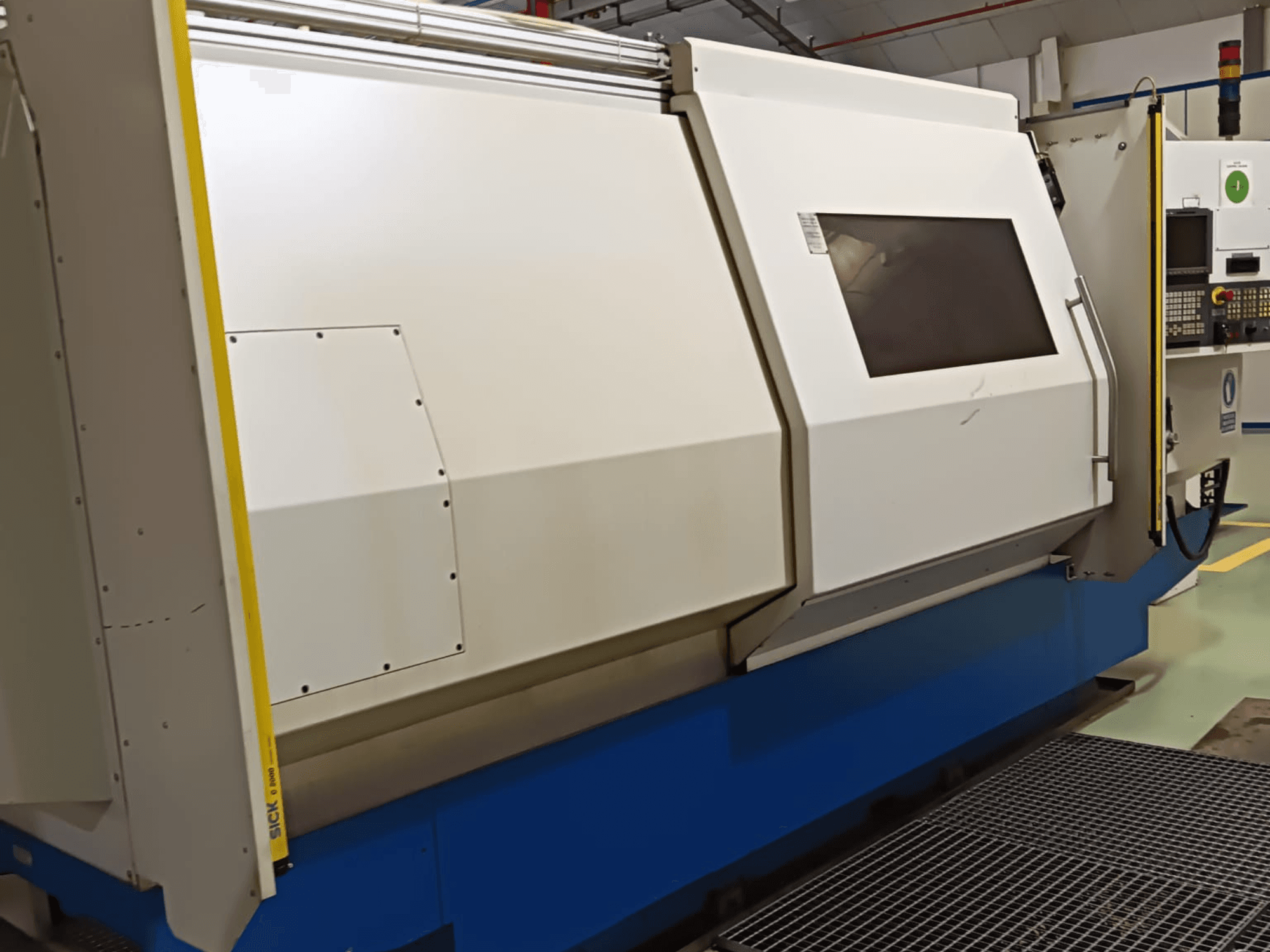 Tööstuslik treipink, külgvaade, millel on suur valge ja sinine korpus, digitaalne juhtpaneel ja turvaelemendid.