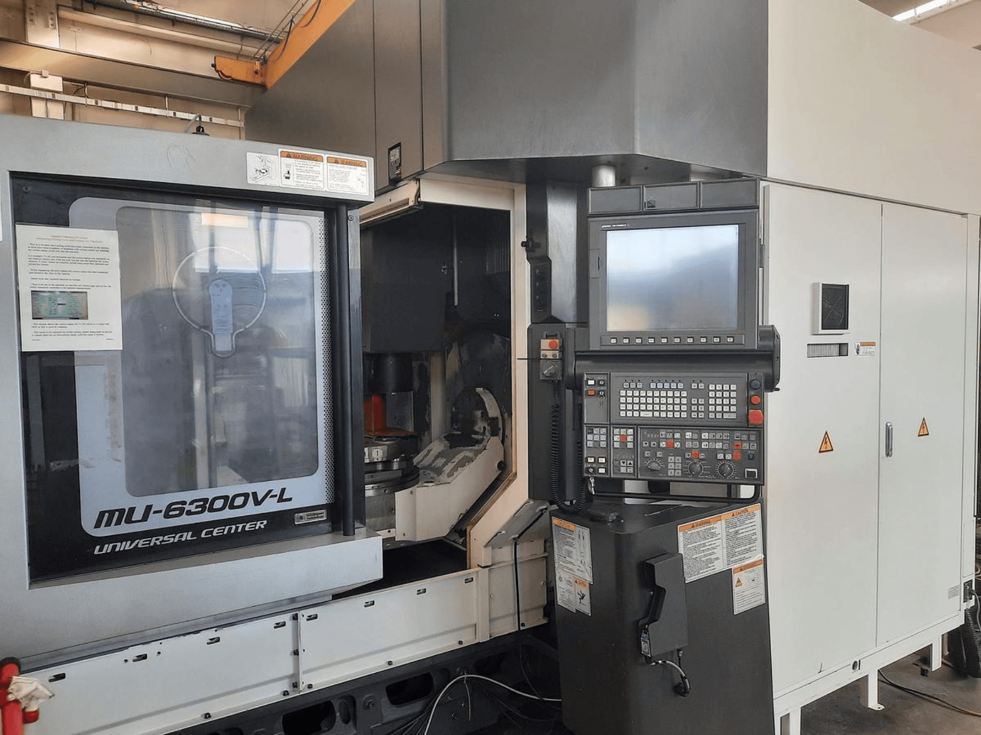 MU-6300V-L universaalkeskuse masin esiplaanil, millel on nähtav juhtpaneel, ekraan ja kasutusjuhend.