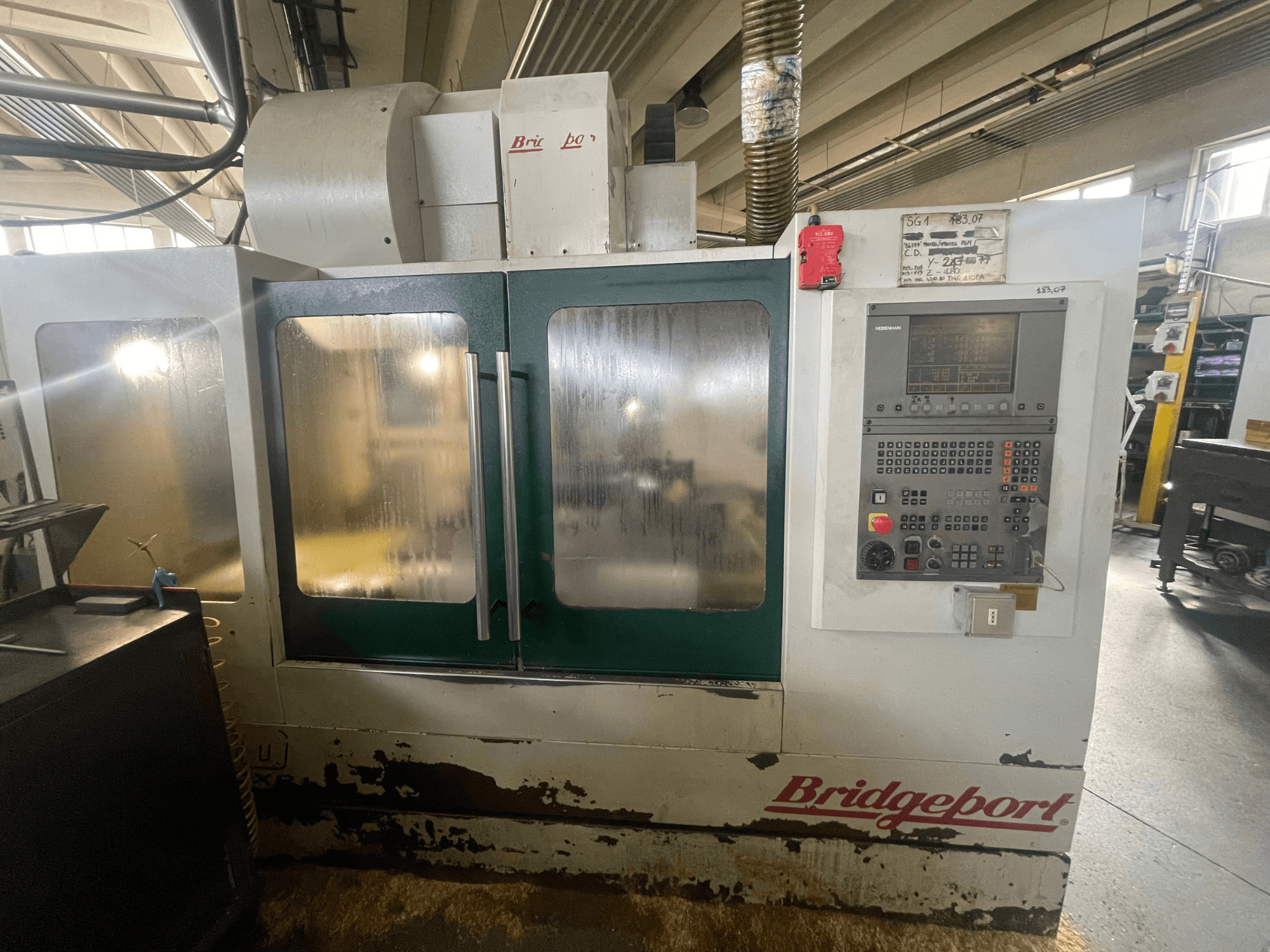 Vertikaalne töötlemiskeskus Bridgeport VMC 1000/30, vaade eest koos juhtpaneeliga, millel on näha kulunud välispind ja rohelised uksed.