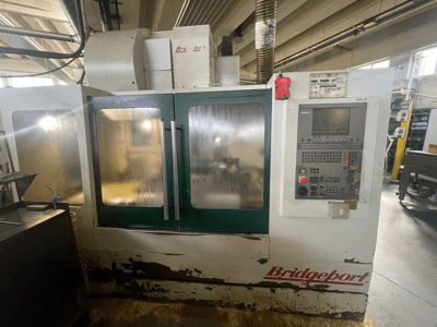 Vertikaalne töötlemiskeskus Bridgeport VMC 1000/30, vaade eest koos juhtpaneeliga, millel on näha kulunud välispind ja rohelised uksed.