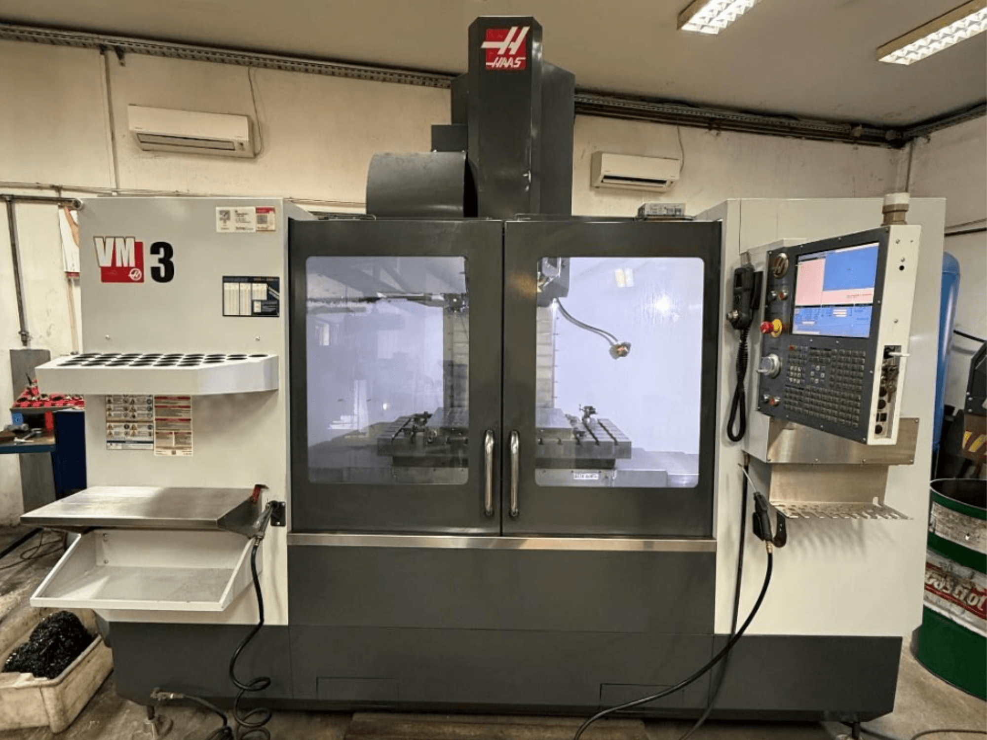 Haas VM-3 vertikaalne töötlemiskeskus eestvaates, millel on suur juhtpaneel ja nähtav töötsoon koos tööriistadega.
