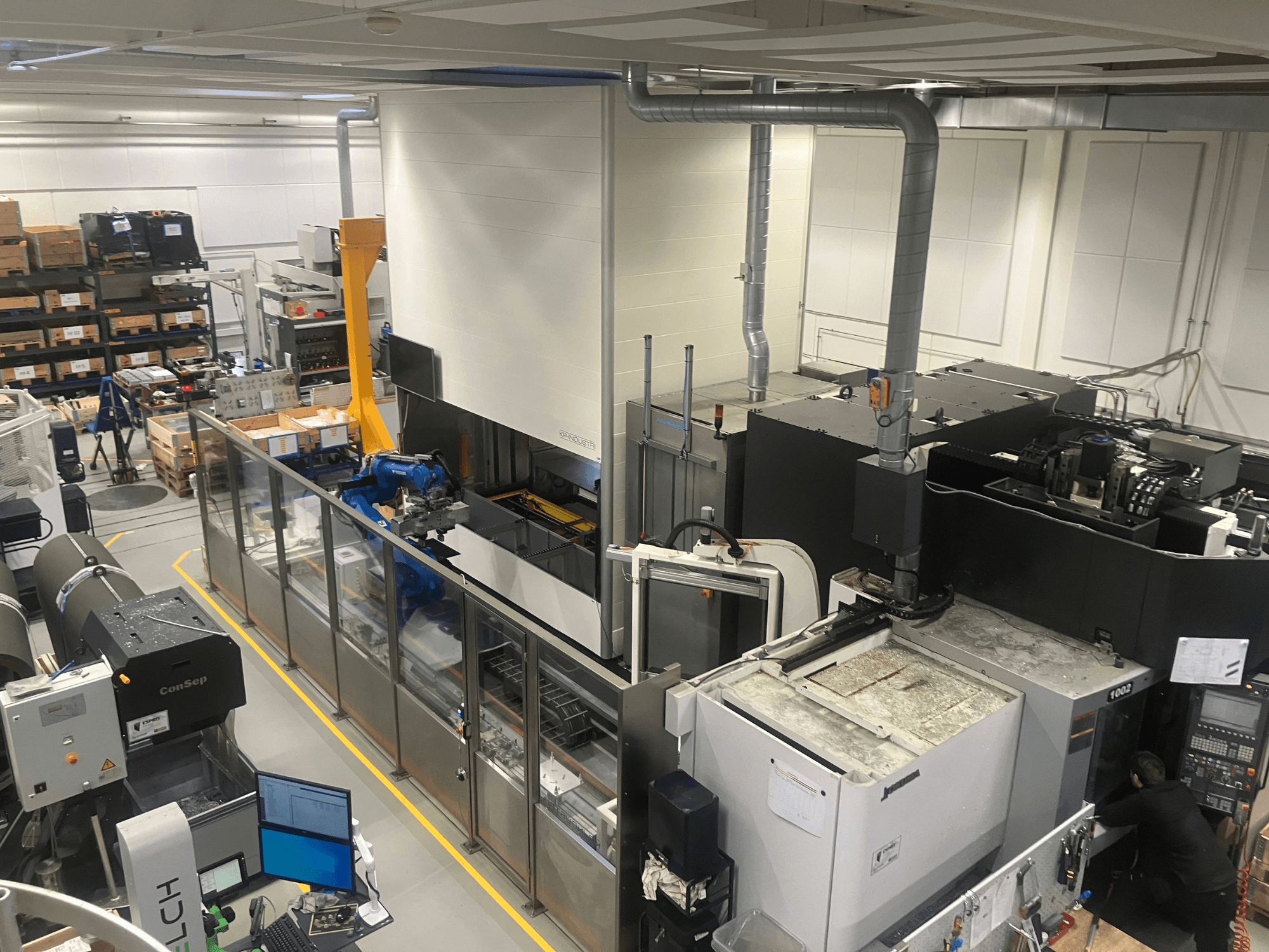 SSI SCHAFER Logimat automaatikasüsteem laos, esiplaanil; robotkäsi, laohoidlad ja masinad.
