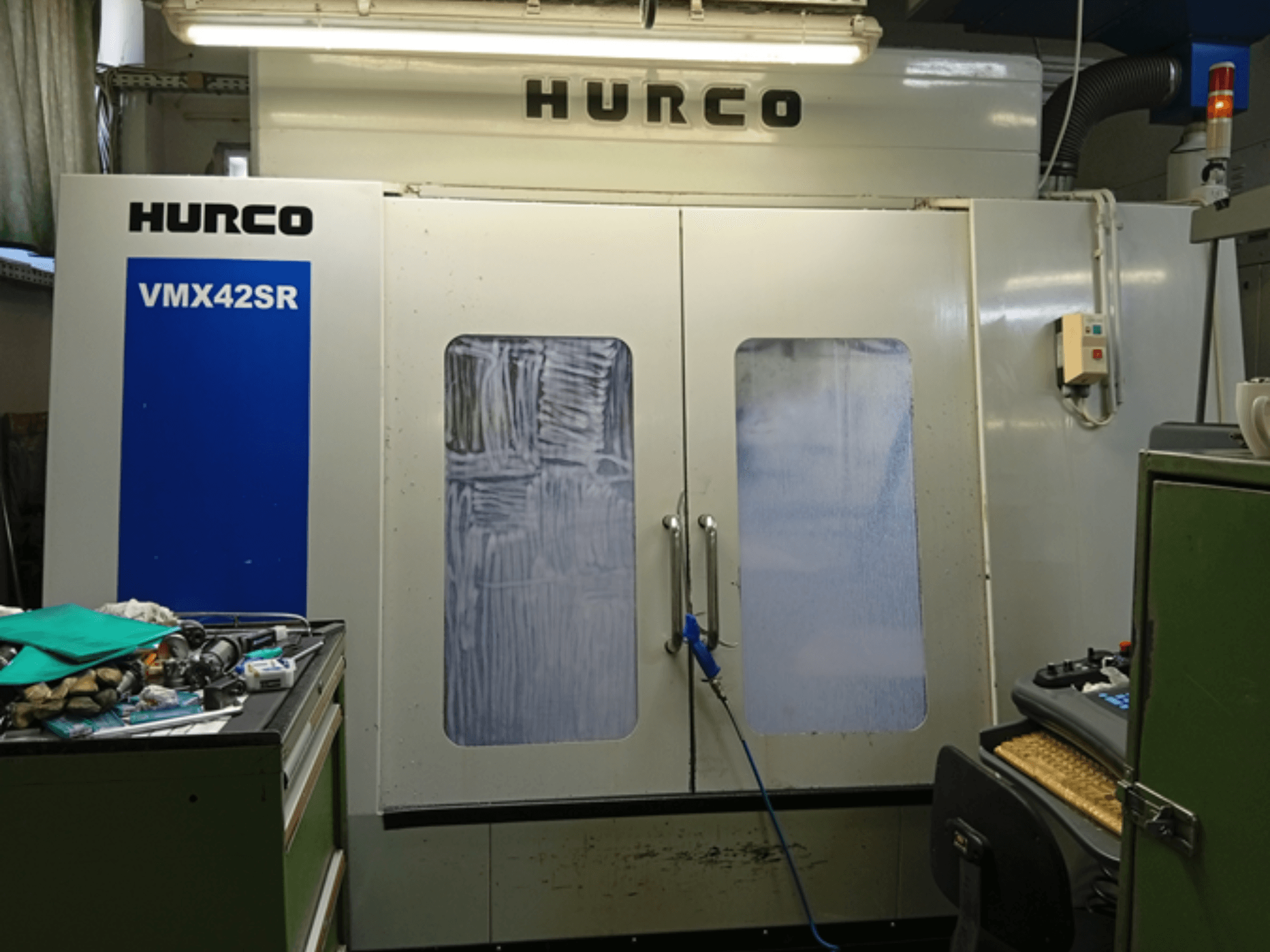 Hurco VMX 42SR vertikaalne töötluskeskus esiplaanil, millel on sinine paneel, juhtimisliides ja puhas tööruum.