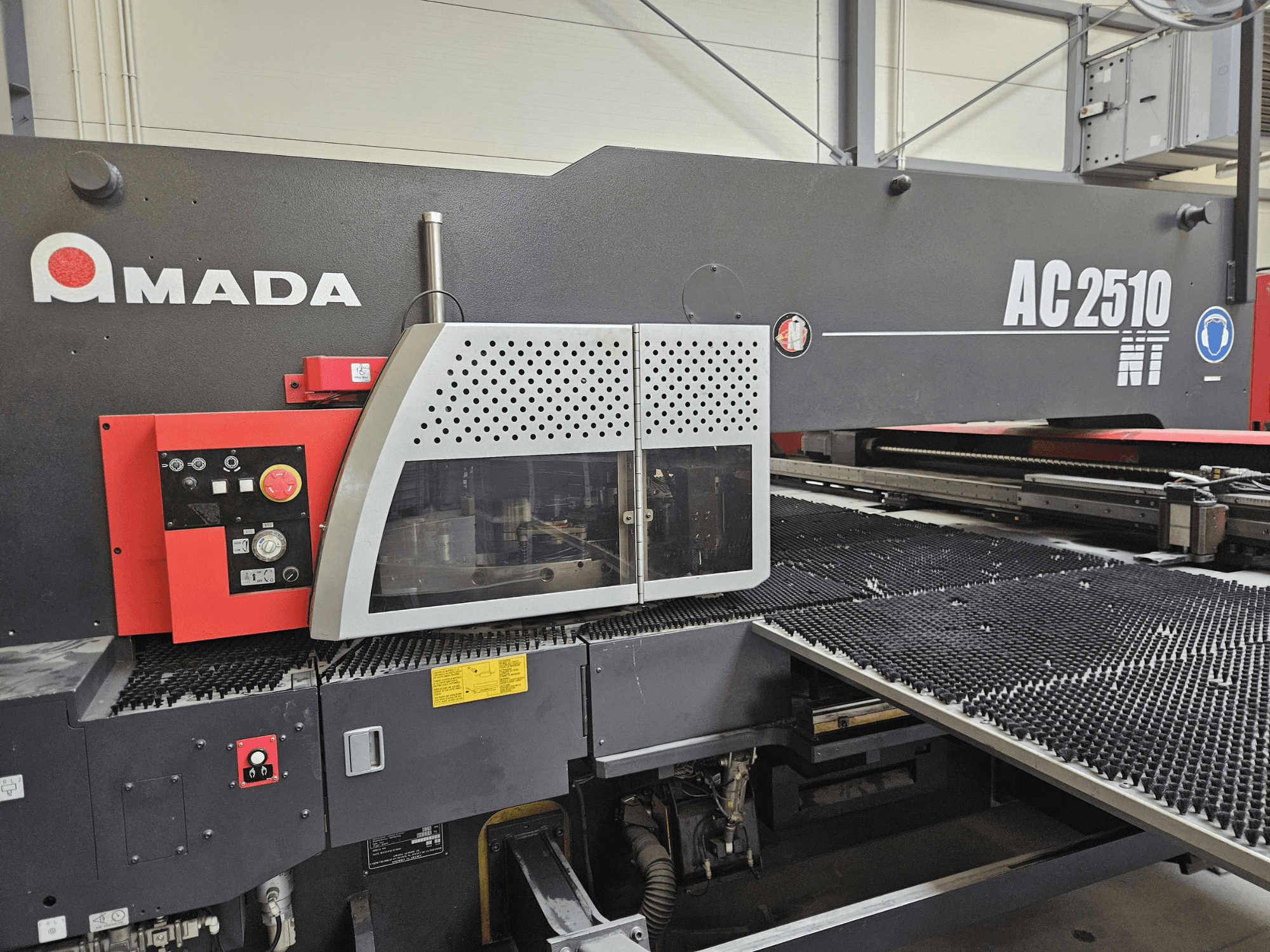 Amada AC2510 NT laserlõikepink, esiplaan, millel on juhtpaneel koos nuppude, nuppude ja turvakattega.
