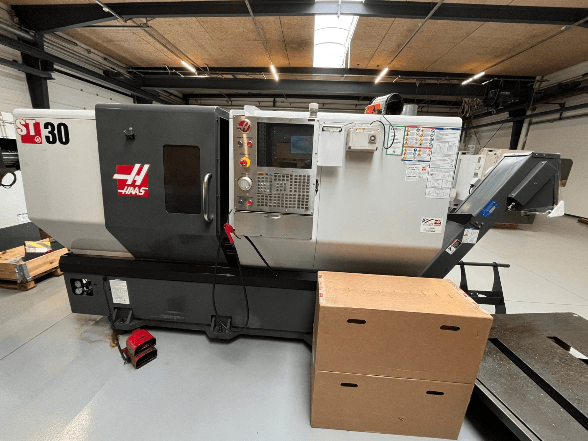 Haas ST-30 CNC-tööpink, esivaade, millel on juhtpaneel nuppudega, hädaseiskamisseadis ja kaks pappkasti üksteise otsas.