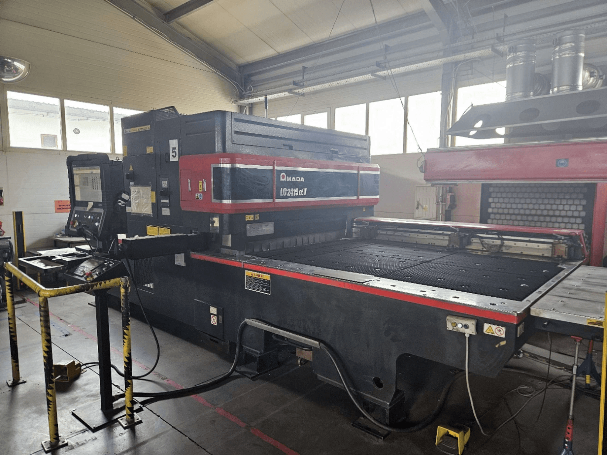 AMADA LC2415 Alpha 5 CO₂-laserlõikepink, esivaade, millel on näha juhtpaneel ja lõikepind koos turvapõrgetega.