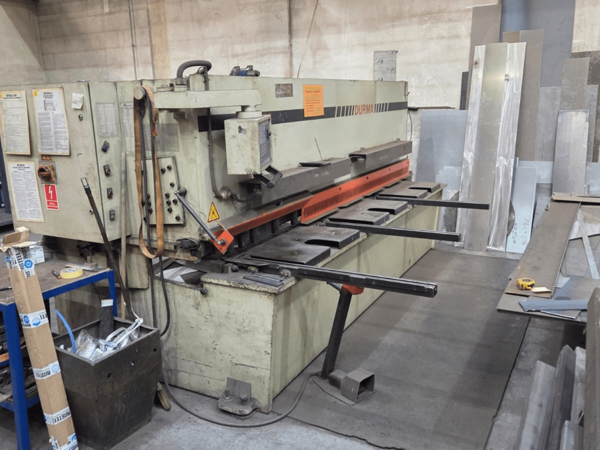 Hüdrauliline lõikepink Durma SB 3060, esivaade, kus on näidatud juhtimisseadmed, lõiketera ja metallplaadid tööruumis.