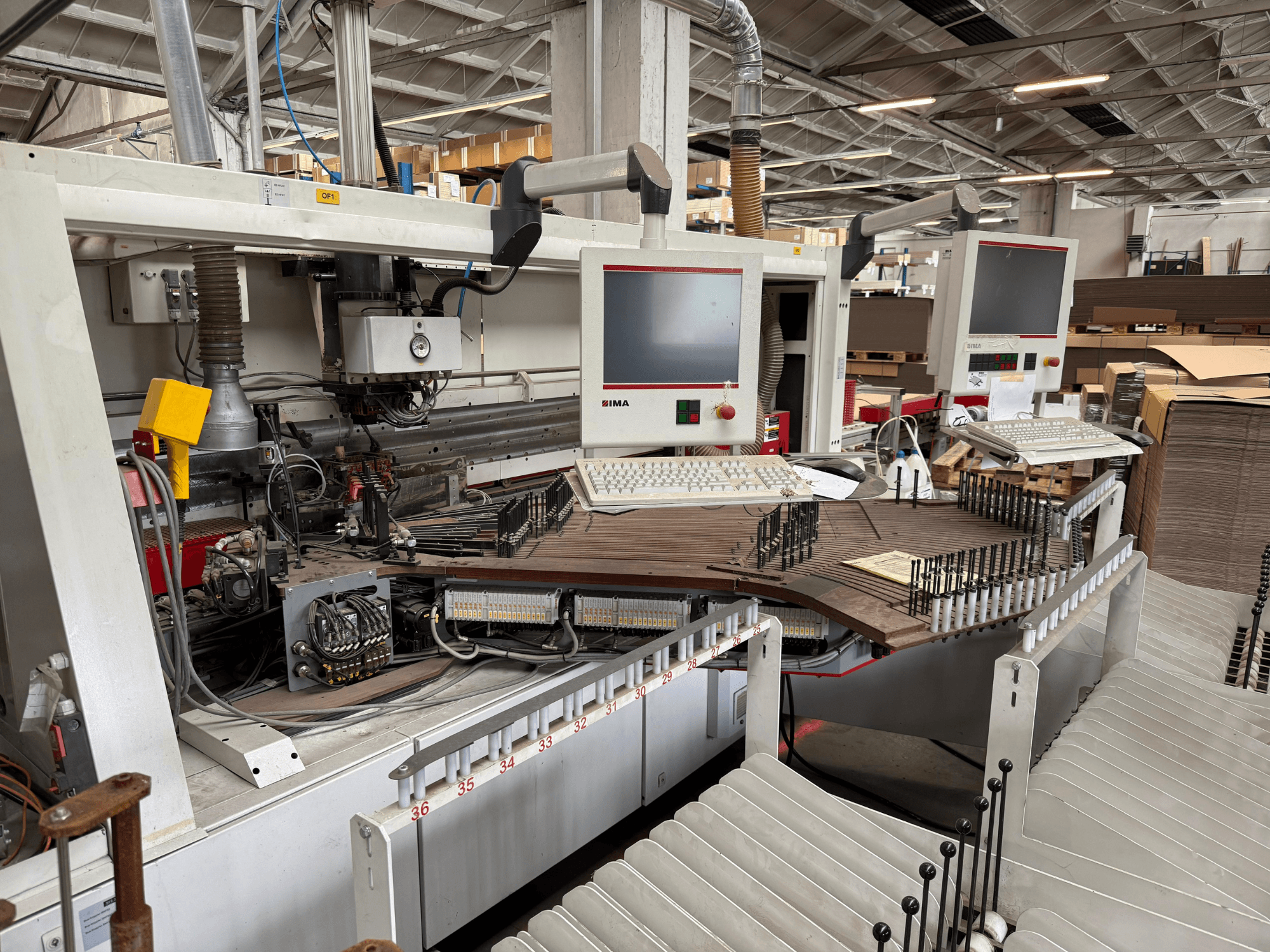 IMA täppispuidutöötlemismasin kahe monitori ja juhtpaneeliga, esiplaanil konveier ja tööriistade ala.