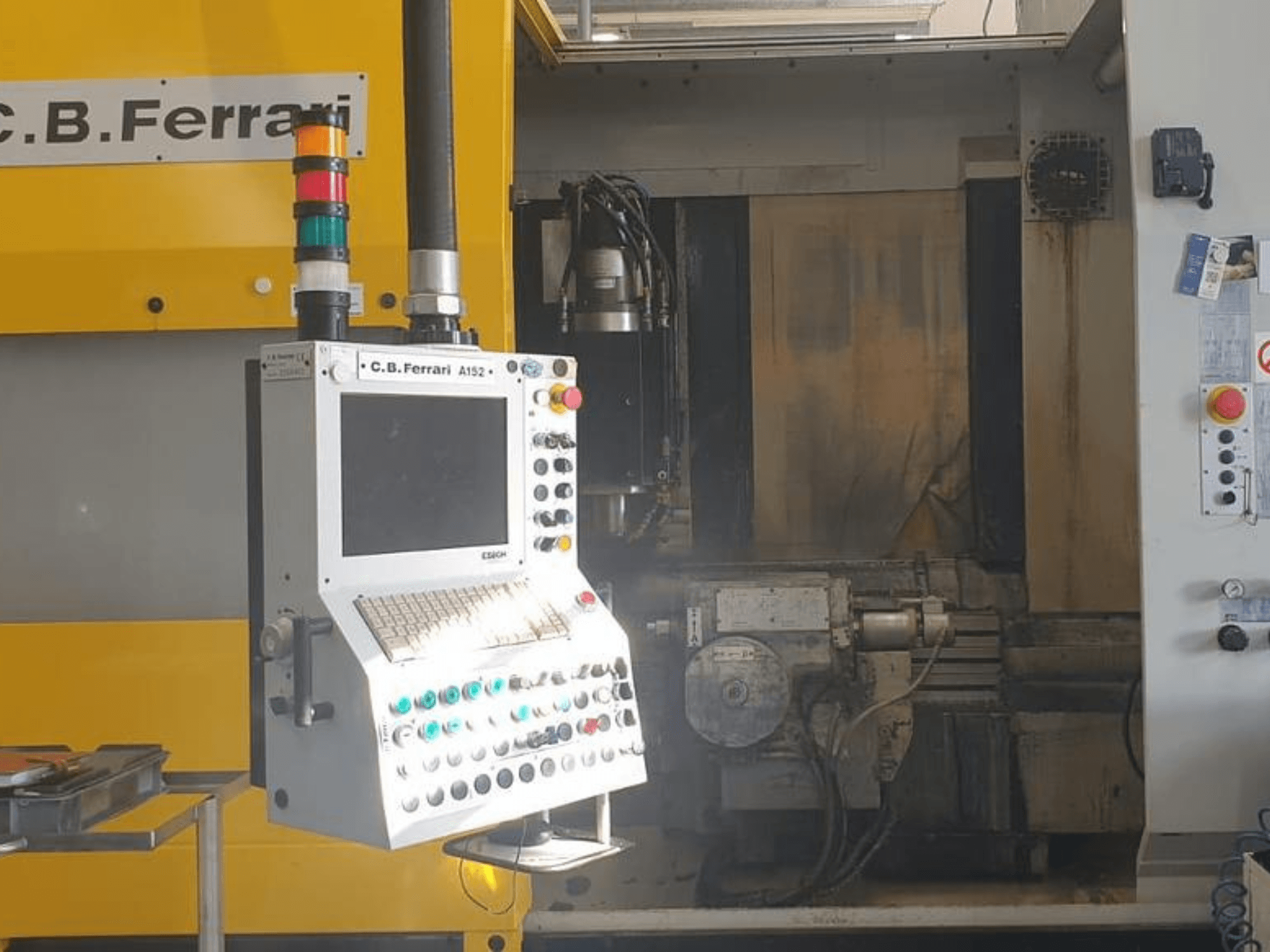 C.B. Ferrari A152 vertikaalne töötlemiskeskus esiplaanil, kus on näidatud juhtpaneel koos nuppude ja masina mootorikomponentidega.
