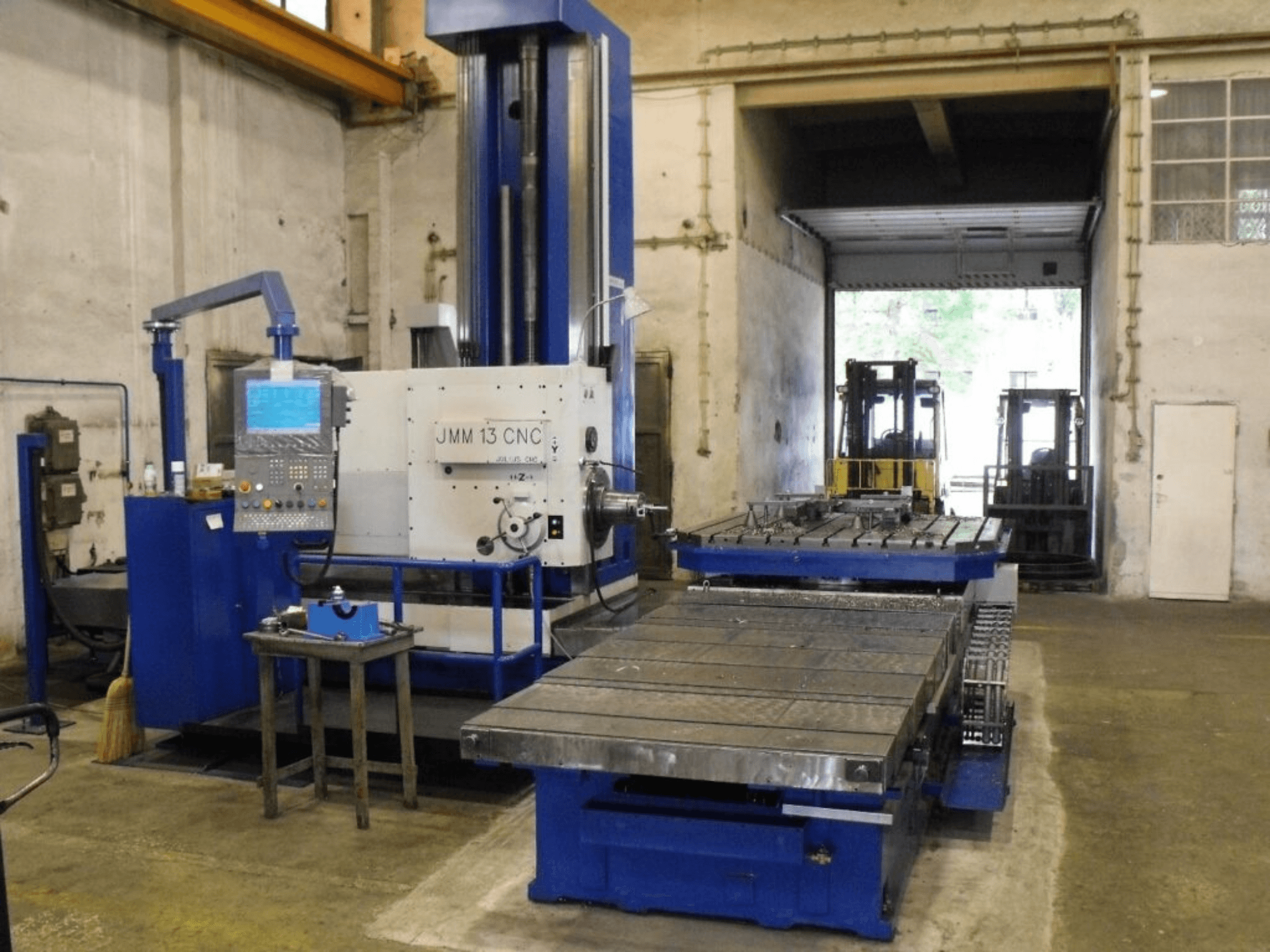 JMM 13 CNC-freesimispink töökojas, esivaade, juhtpaneel, suur töölaud ja tööstuslik taust.