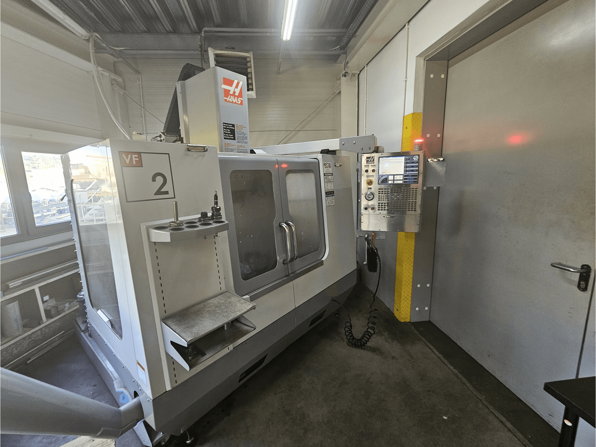 Haas VF-2 CNC-freesping, esivaade, kus on näidatud juhtpaneel, tööriistahoidjad ja selge aken tööruumile.