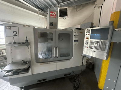 Haas VF-2 CNC-tööpink, esiplaanil, kus on juhtimisseadmed, tööriistahoidja ja läbipaistvad uksed, kus on näha tööriistad kapi sees.