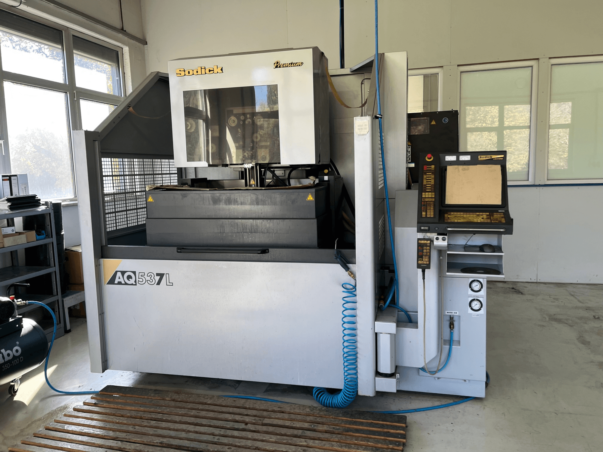 Sodick AQ537L elektritöötlusmasin (EDM) esiplaanil, kus on juhtpaneel, veejahutusliinid ja tööruum.