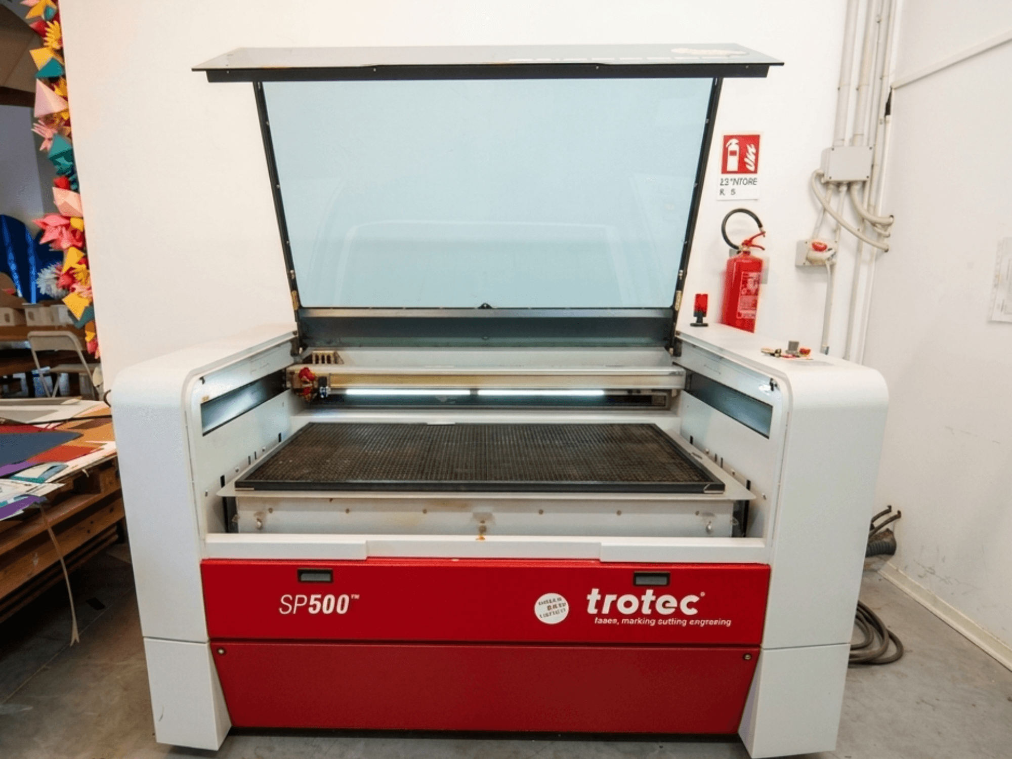 Trotec SP500 C200 lasergraveerimismasin esiplaanil, avatud kaanega, mis näitab tööala ja juhtimisseadmeid.