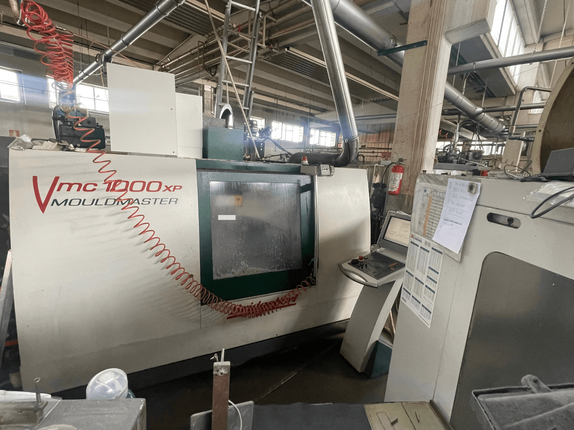 Vertikaalne töötlemiskeskus Bridgeport VMC 1000, vaade eest, millel on näha juhtpaneel ja masina detailid tööstuslikus keskkonnas.