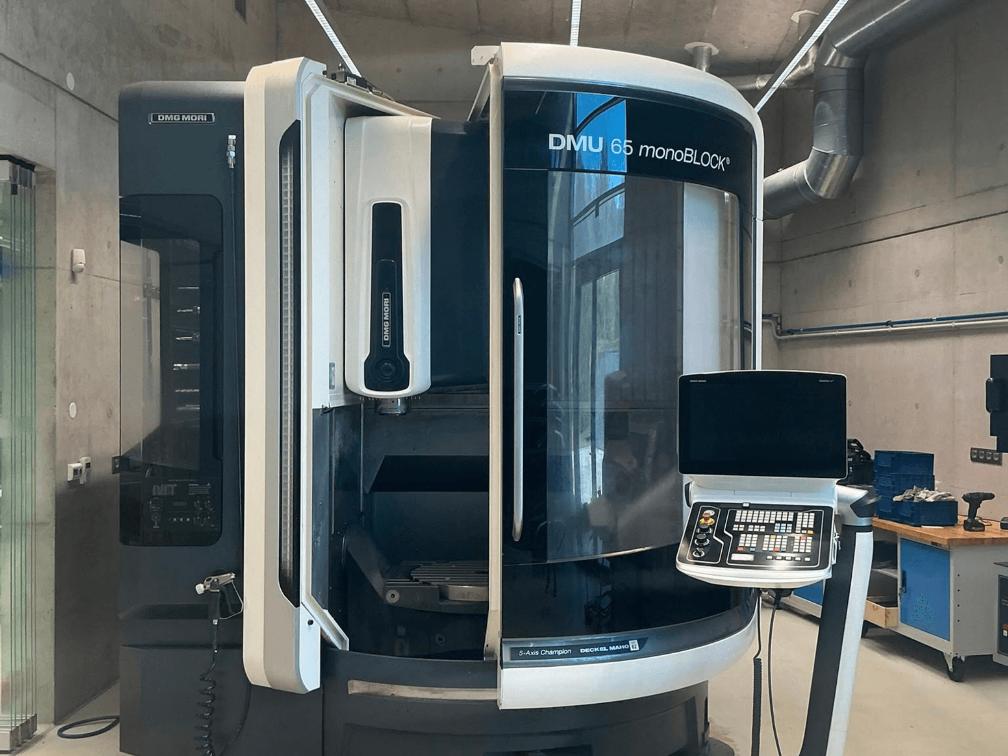 DMG MORI DMU 65 monoBLOCK vertikaalne töötlemiskeskus, vaade eest, millel on näha juhtpaneel ja masina detailid töökoda keskkonnas.