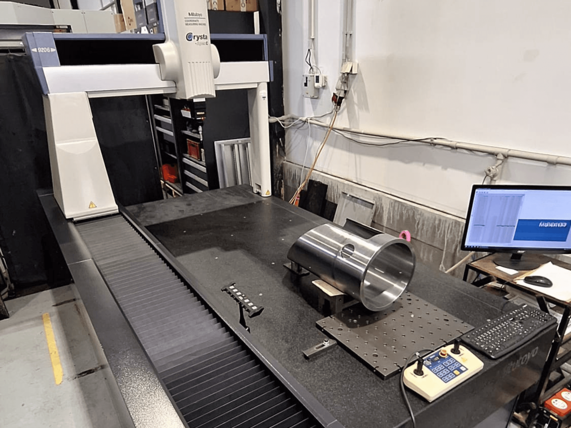 Mitutoyo Crysta-Apex C9206 CMM esiplaanil, mõõtes silindrilist metalldetaili mustal graniidist pinnaplaadil.