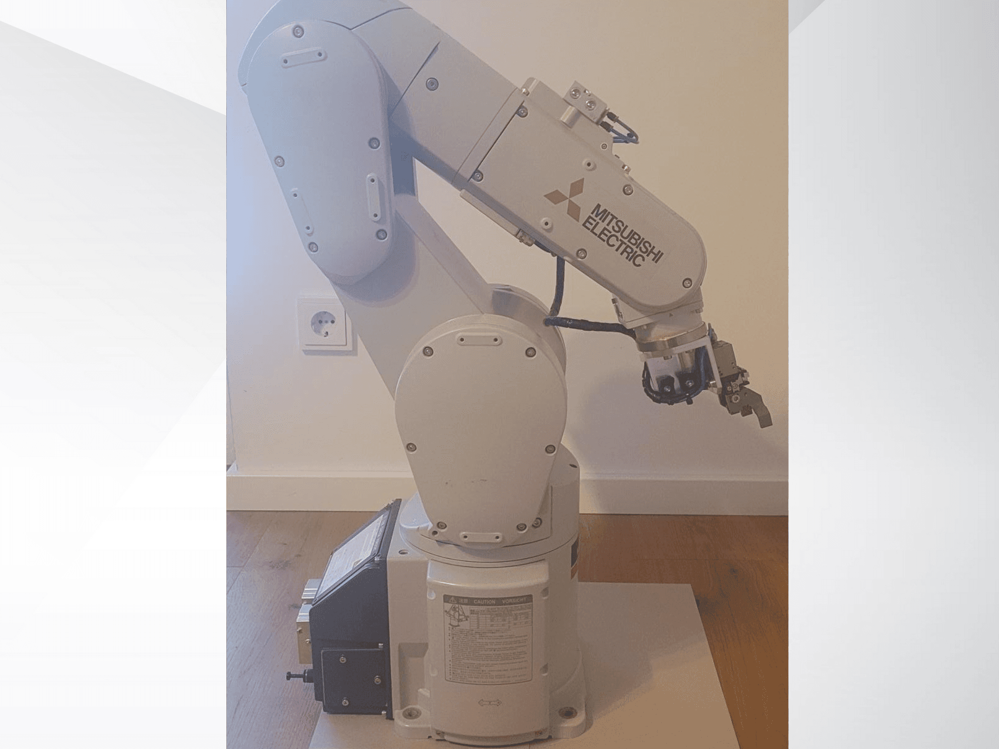 Mitsubishi Electrici robotkäsi, külgvaade, millel on haarats ja üksikasjalik juhtpaneel aluspinnal tööseadete jaoks.