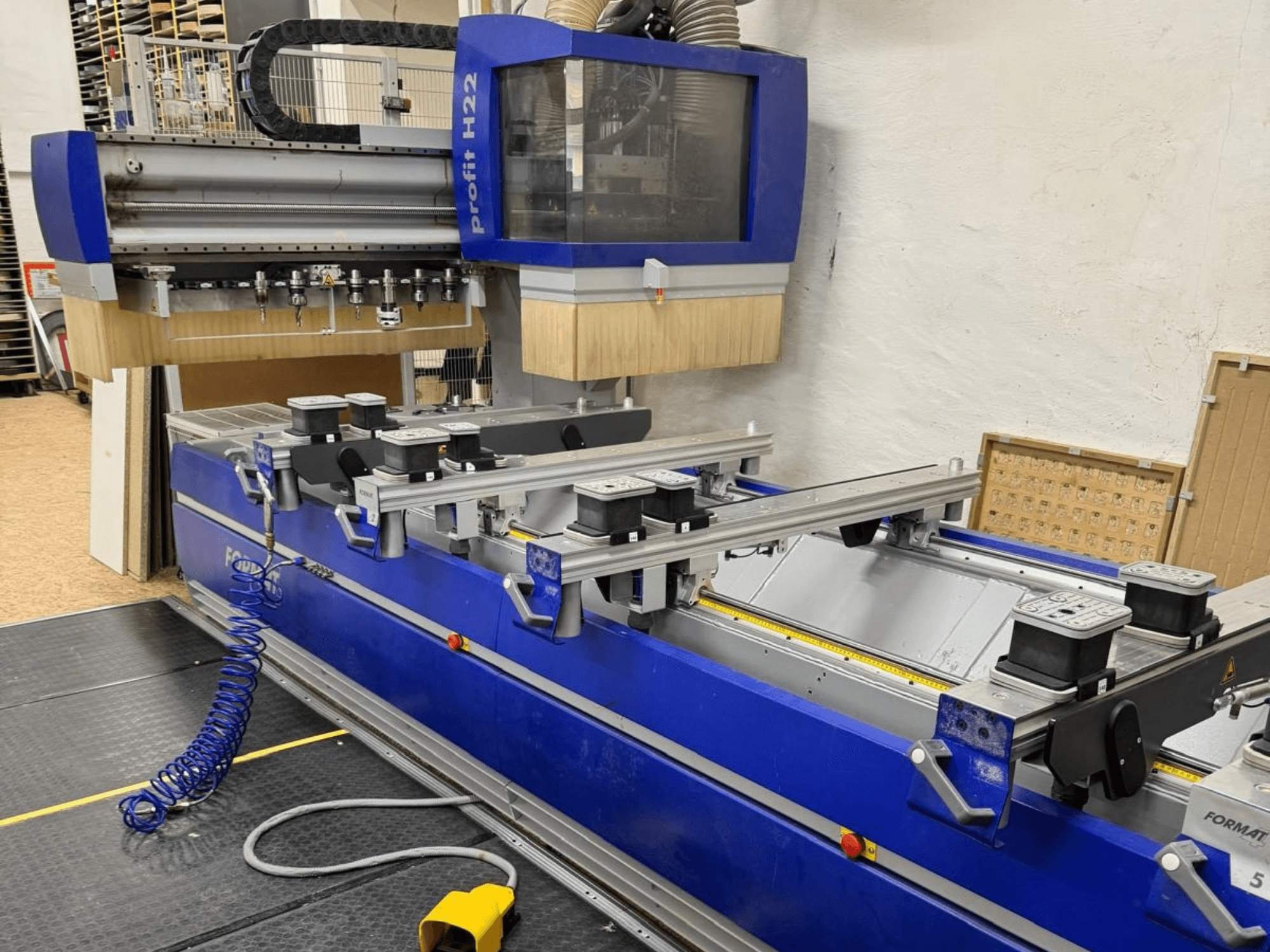 FORMAT4 PROFIT H22 CNC-puidutöötluskeskus, vaade eest, sinisel korpusel on näha töötlusriistad ja kinnitusklambrid.