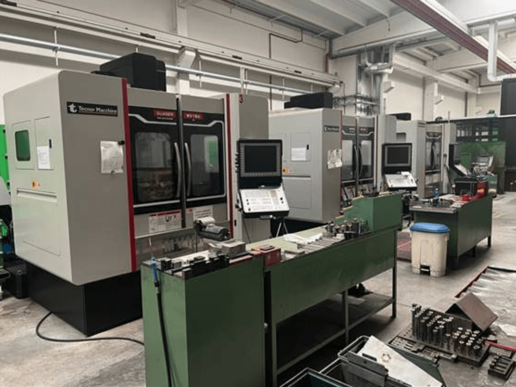 Neli Tecnoer Marchine'i CNC-tööpinki töökojas, esiplaanil, tööriistad ja detailid rohelistel tööpinkidel.