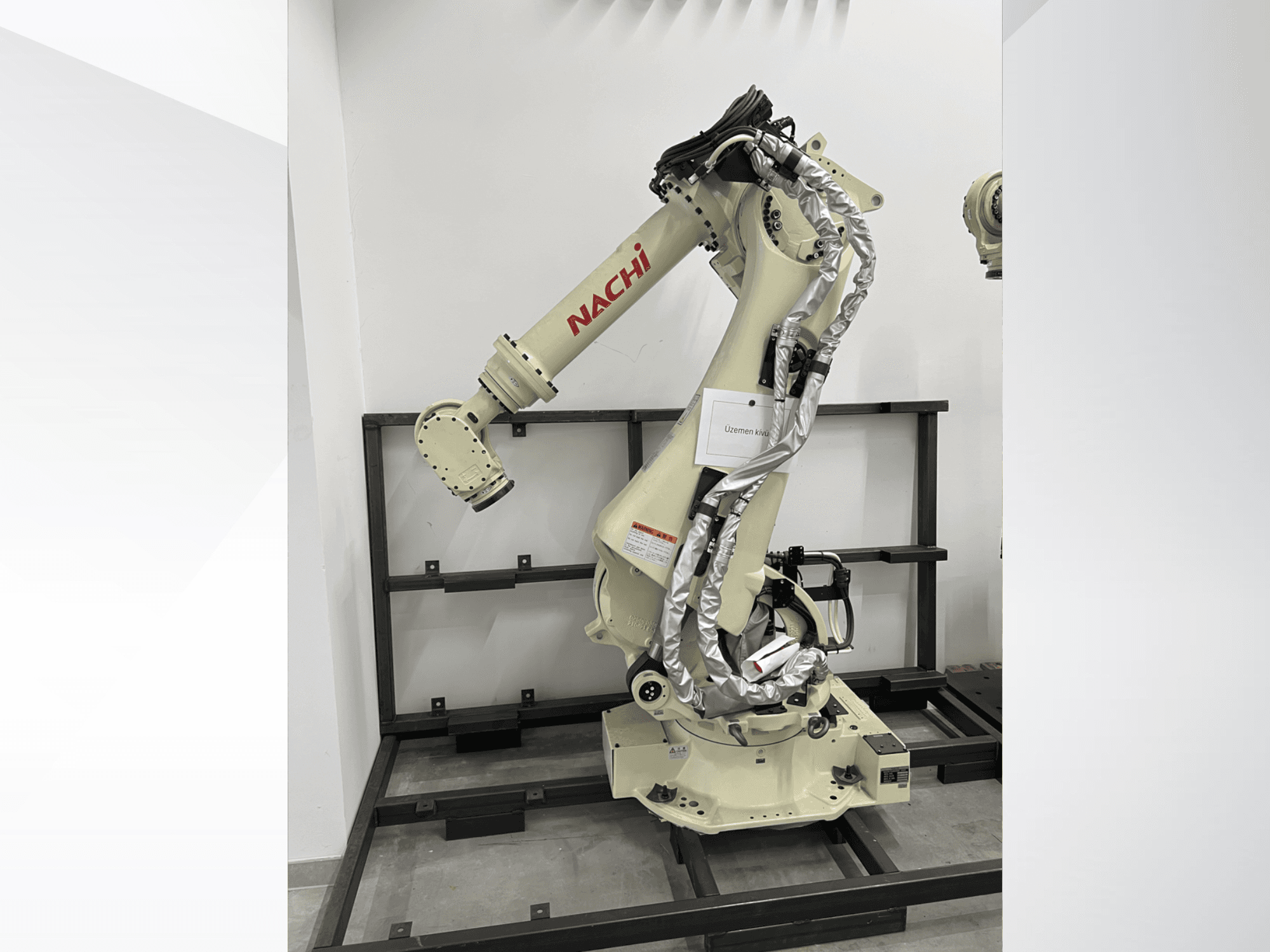 NACHI SRA166-01 robotkäsi külgvaates, millel on painduvad liigendid, kinnitatud kaablid ja paigaldatud kaitseraamile.