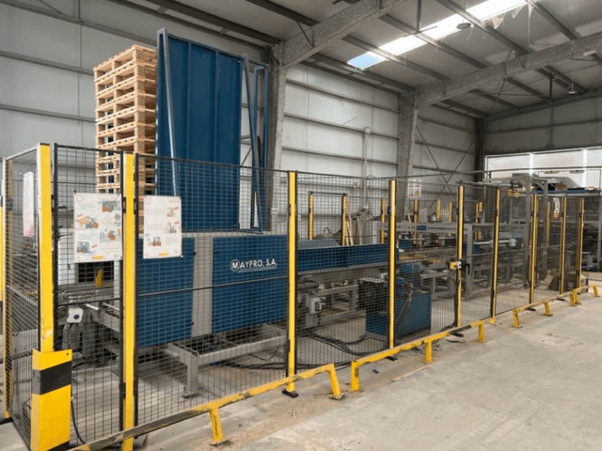 Maypro S.A. tööstuslik kaubaaluste pakkimismasin laos, millel on turvavõrk ja juhtimisseadmed, külgvaade.