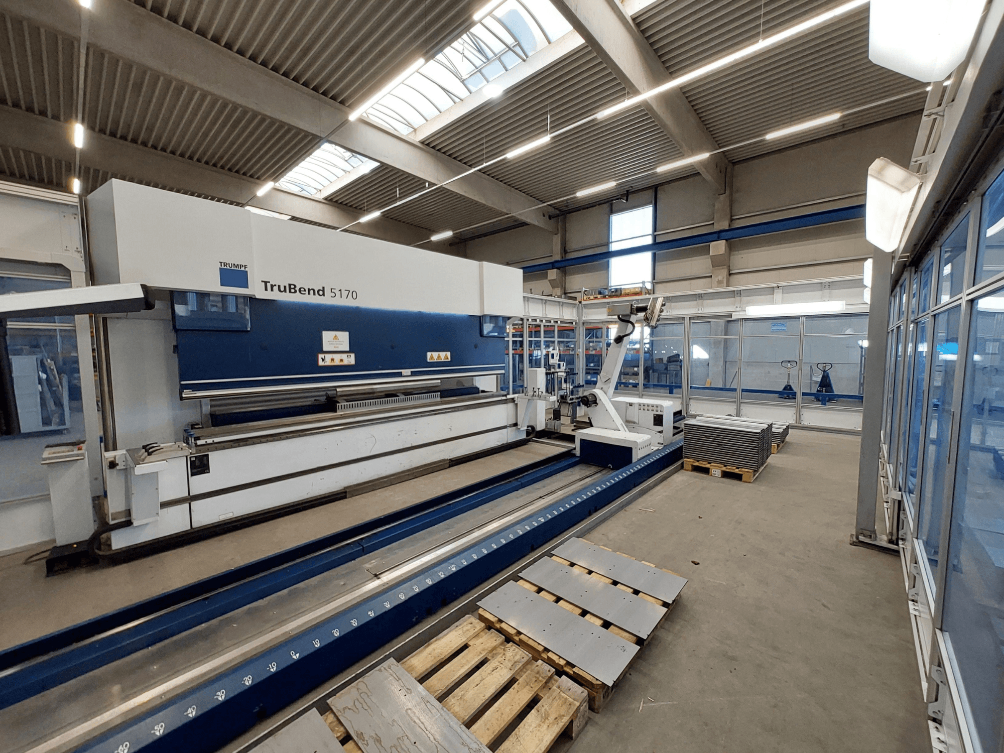 TRUMPF TruBend 5170 presspink töökojas, külgvaade, kus on näha painutusinstrumendi ja kaubaalustel virnastatud metallplaadid.