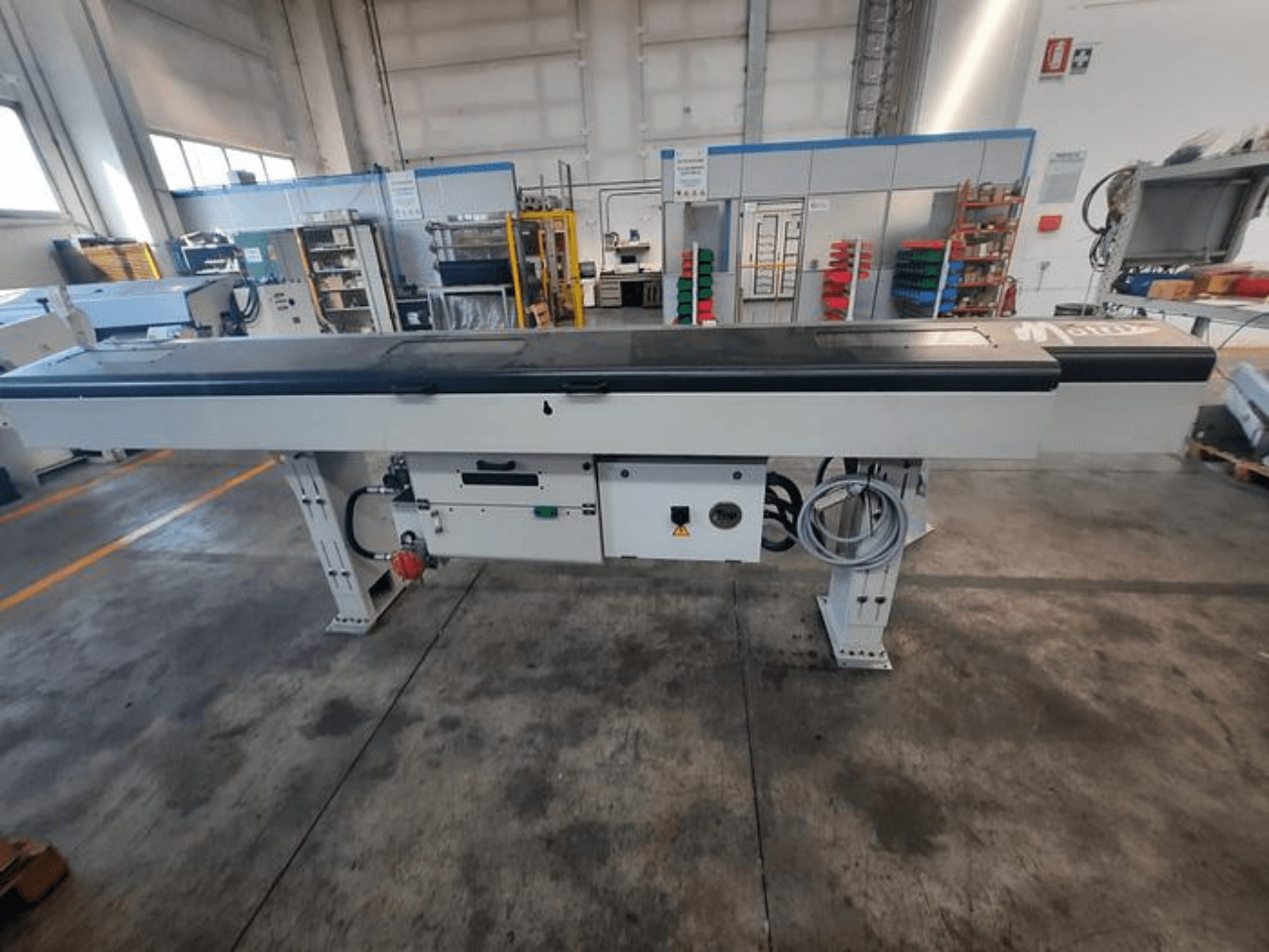 Metallkonveierilaua sileda musta pealispinnaga, külgvaates, millel on juhtnupud ja kaablid; osaliselt nähtav kaubamärgi logo.