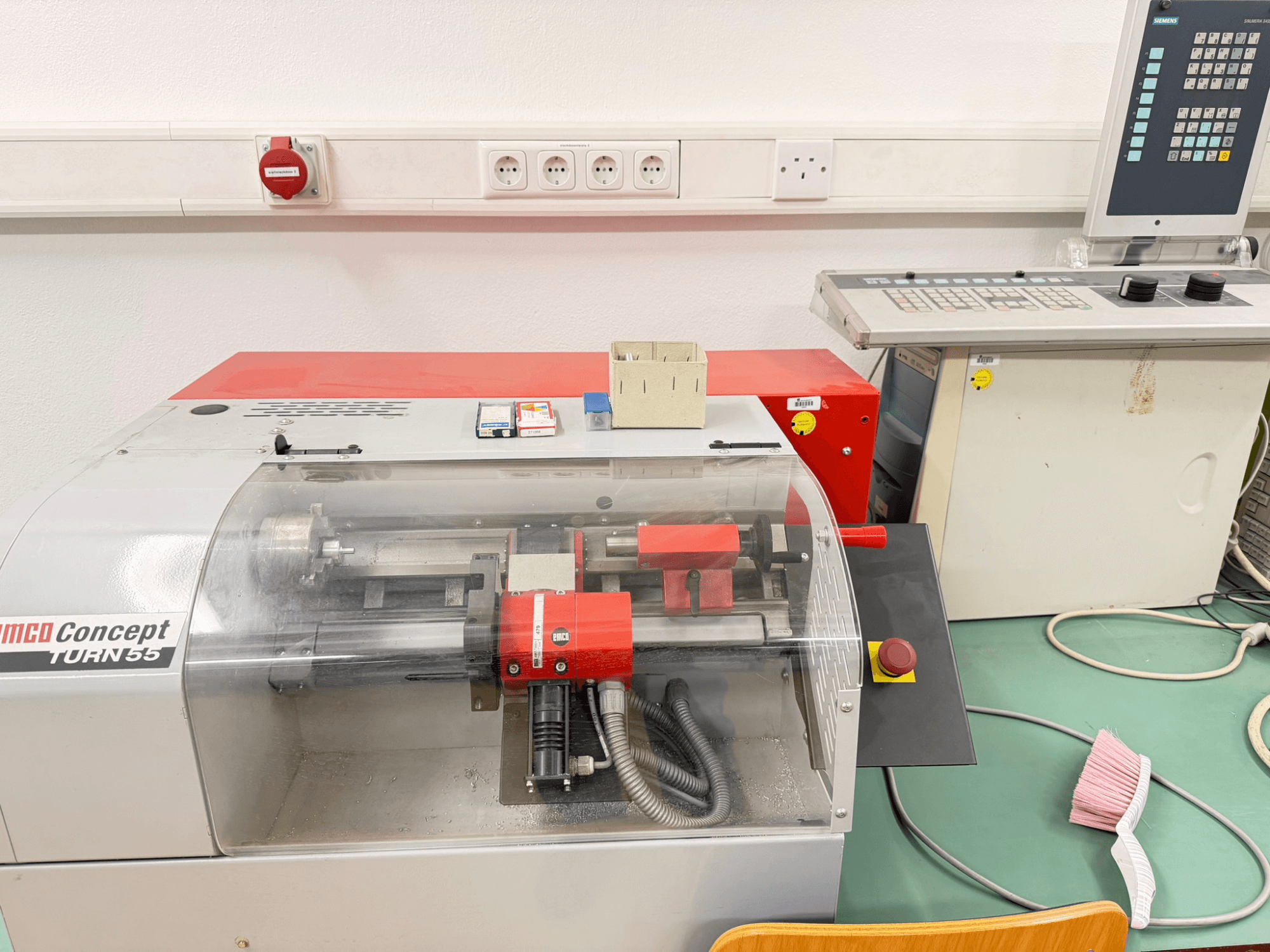 EMCO Concept Turn 55 punase ja halli väliskujundusega horisontaalne treipingi, esiplaanil on näidatud juhtimisseadmed ja tööpiirkond.