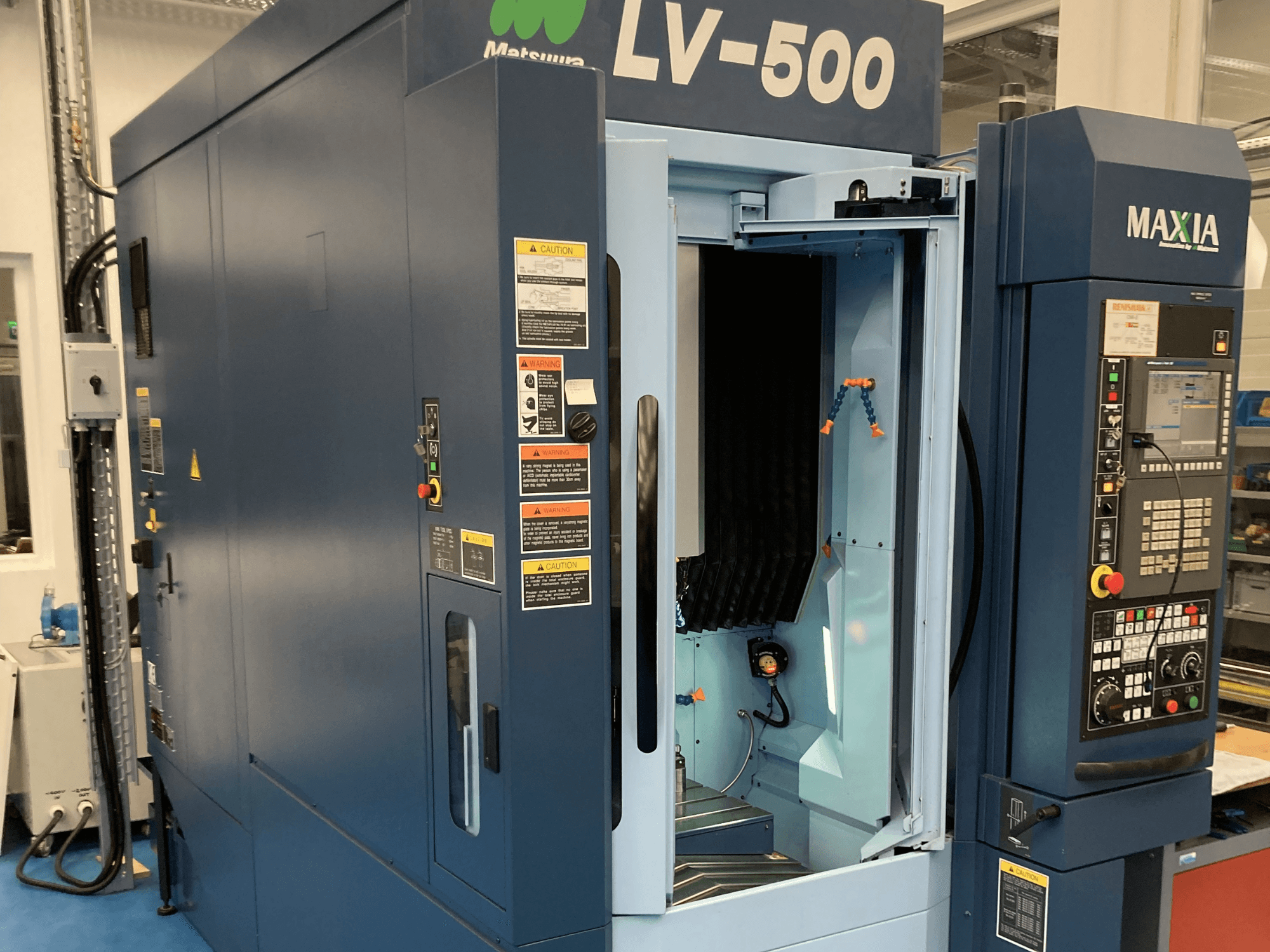 Matsuura LV-500 vertikaalne töötluskeskus esiplaanil, millel on avatud uks ja nuppudega juhtpaneel.